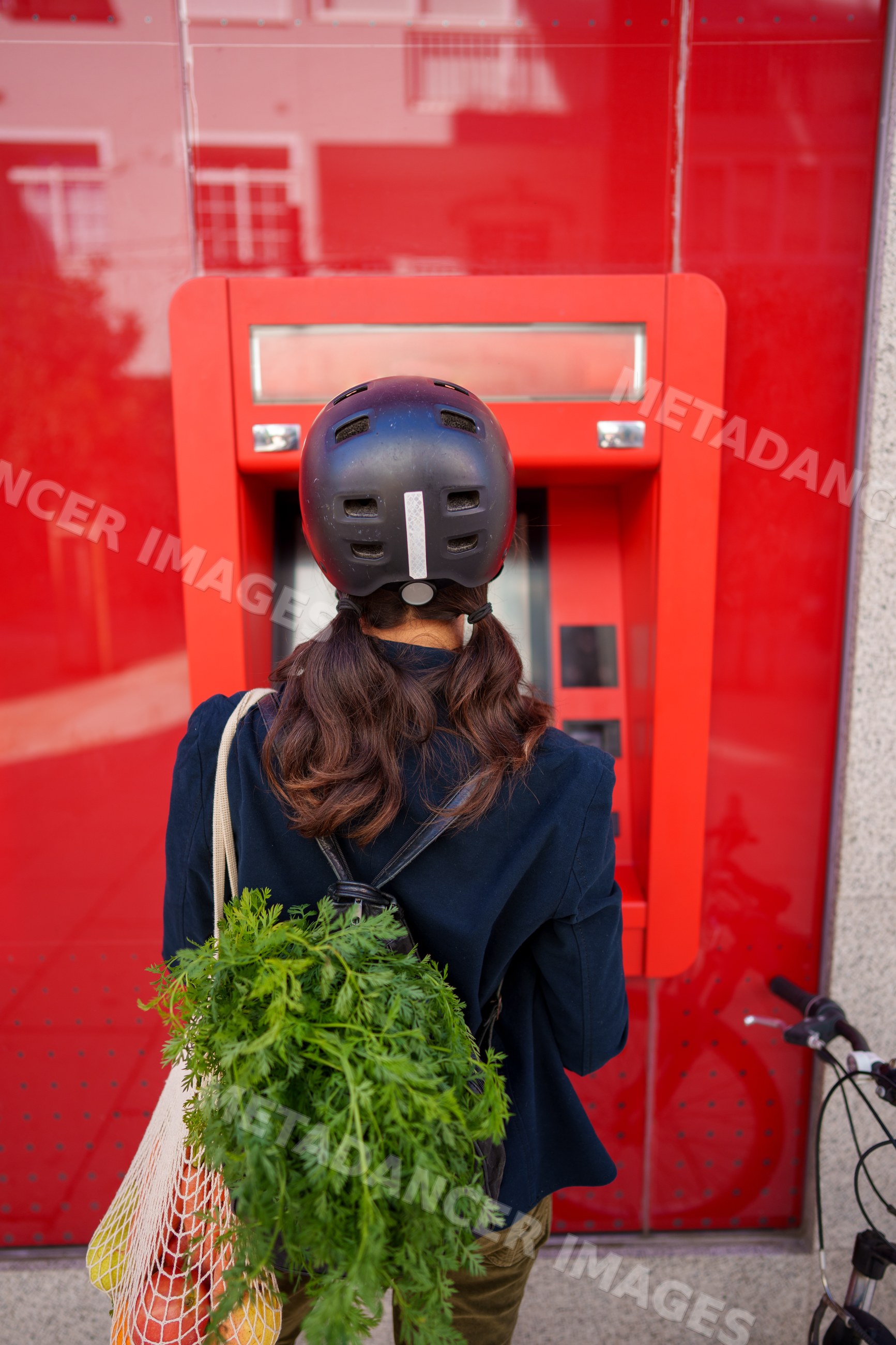 Hispanic woman using an atm outdoors with bicycle and groceries
