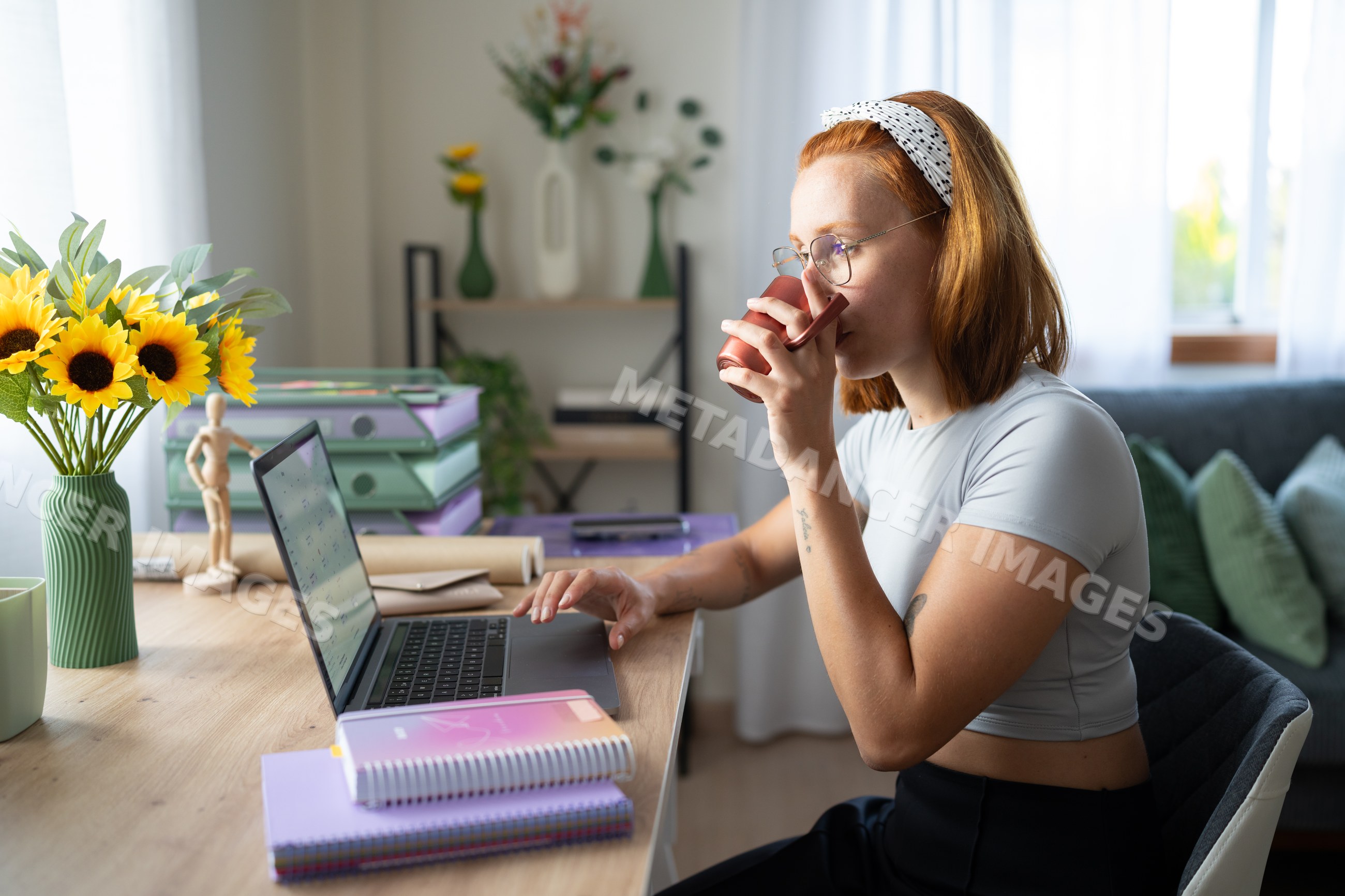 A white woman drinks coffee while working on her laptop at home