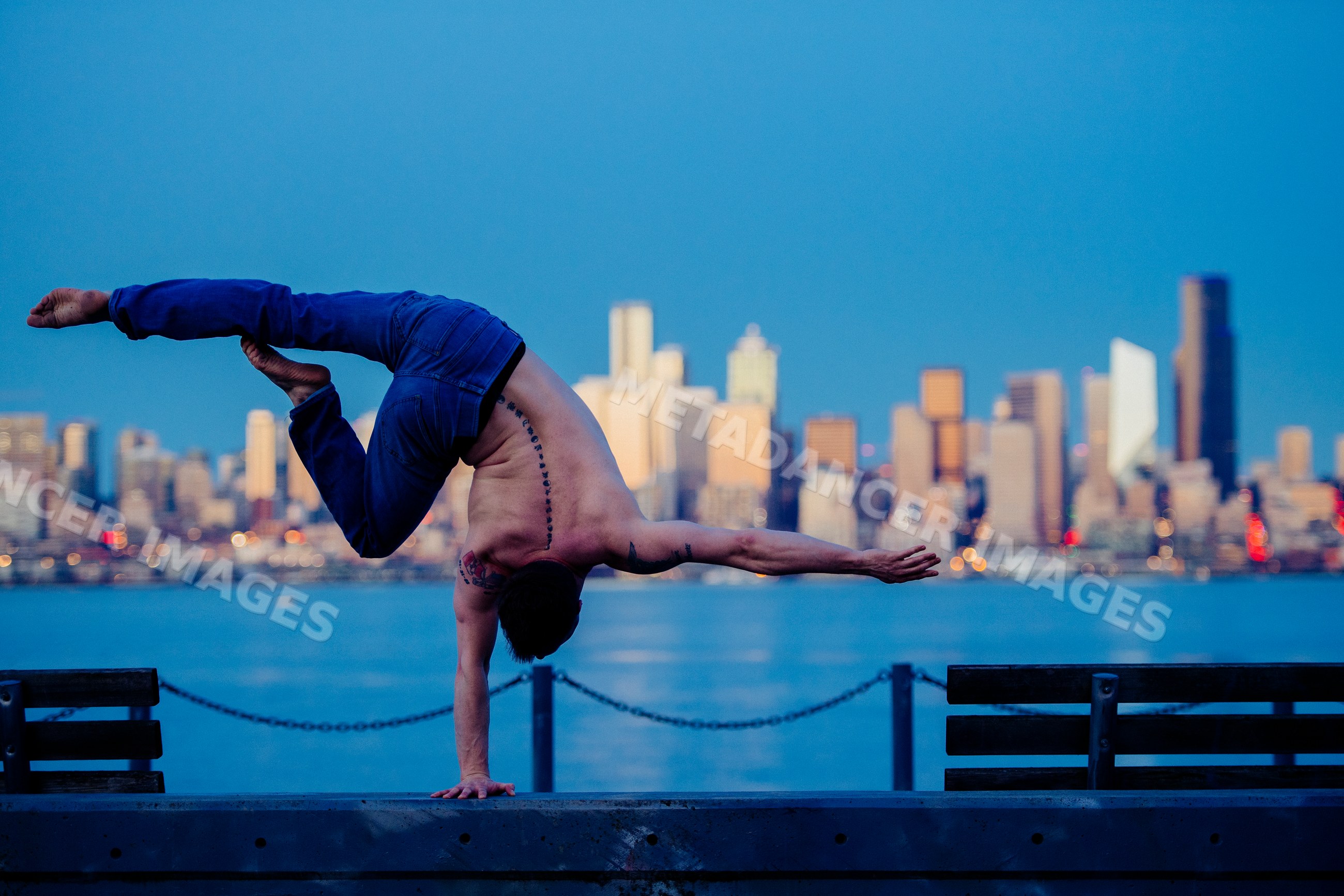 White man practicing one-hand yoga handstand at Seattle waterfront