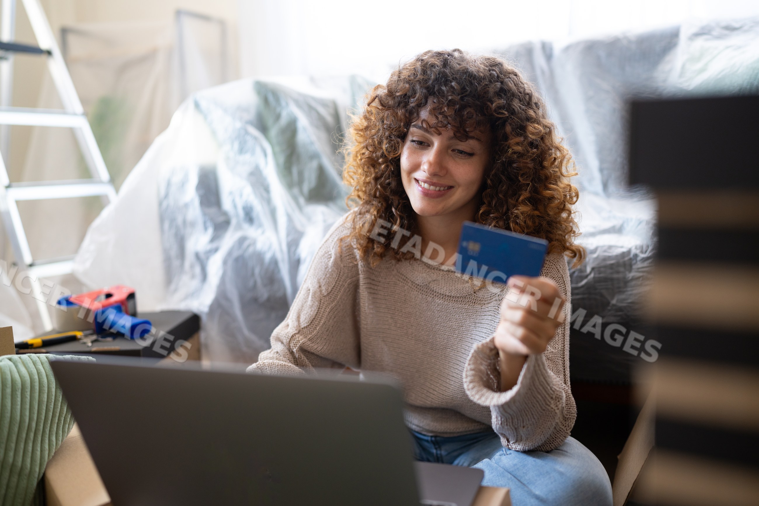 White woman holding credit card and using laptop indoors amid moving