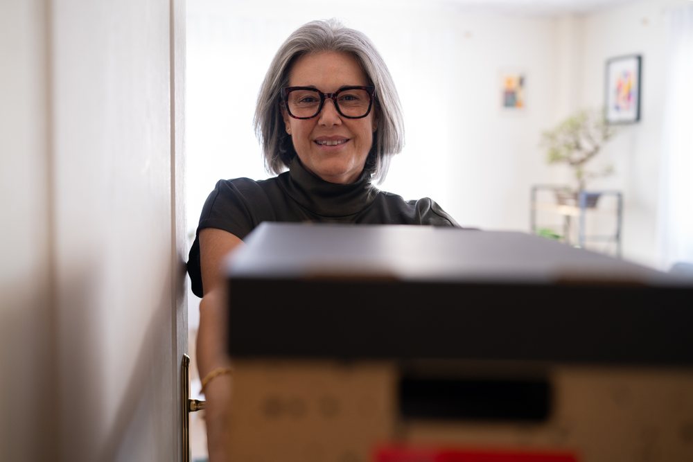 White woman holding black box in doorway inside modern home interior