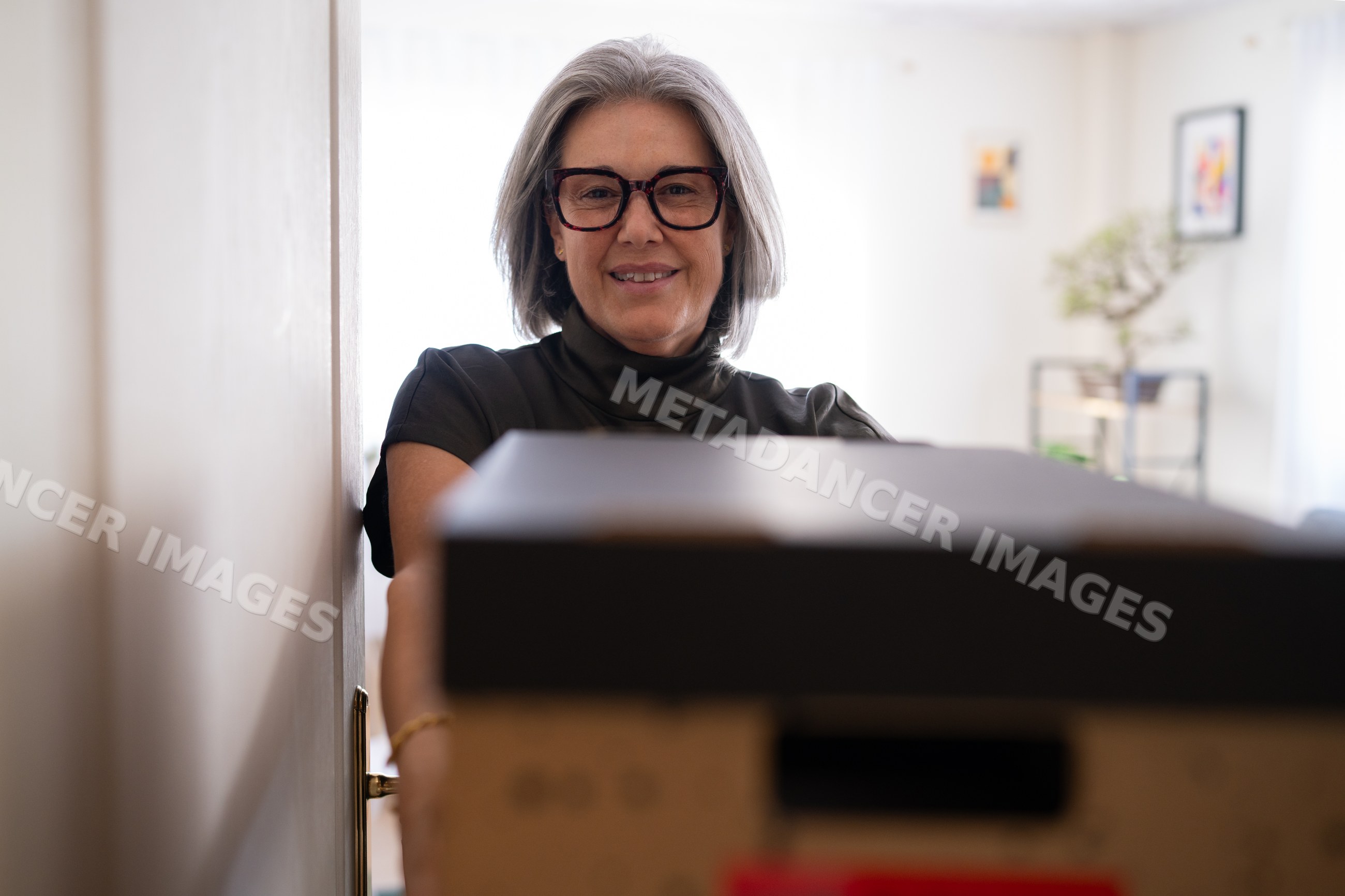 White woman holding black box in doorway inside modern home interior
