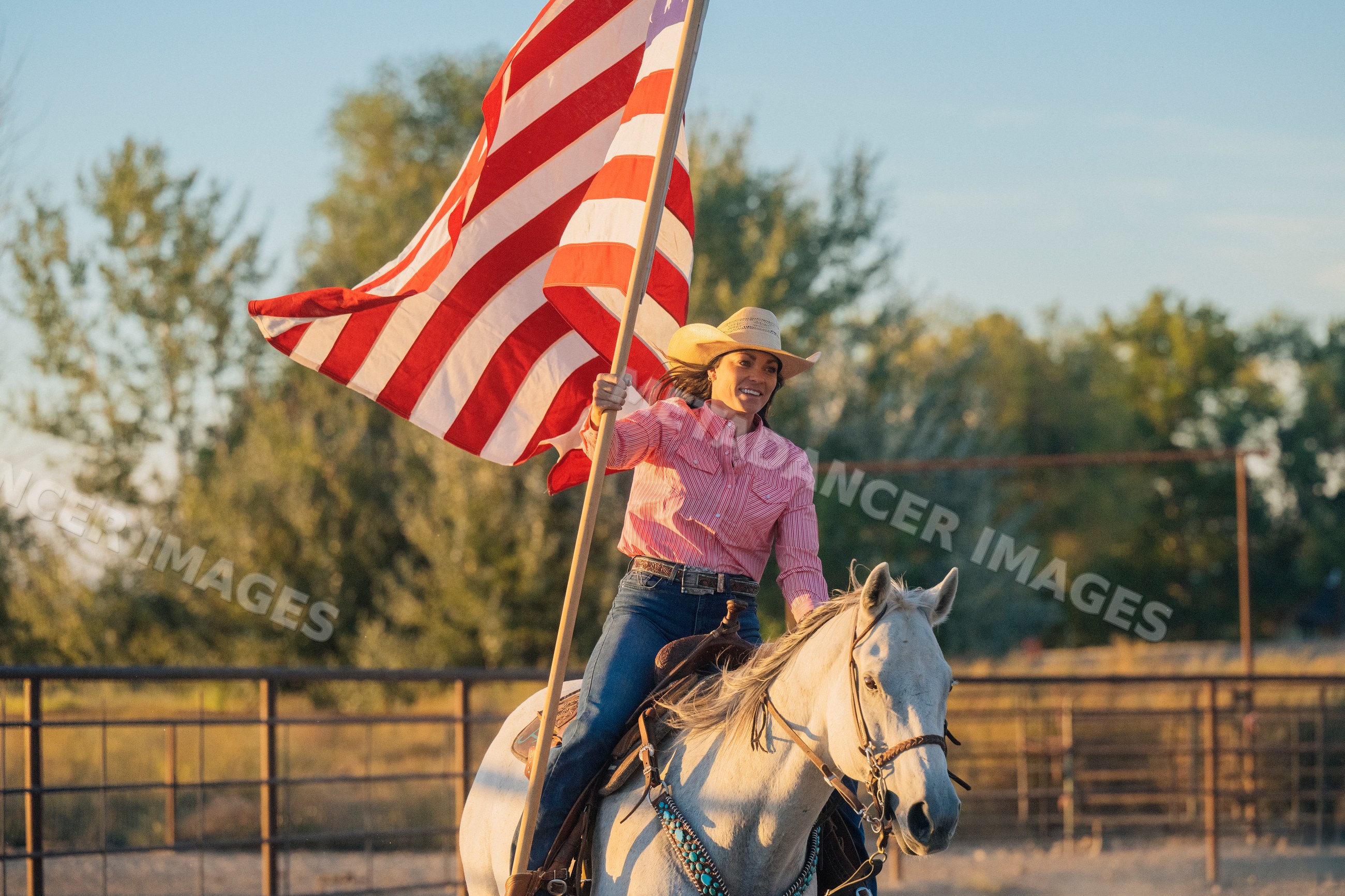 Woman riding white horse holding american flag outdoors