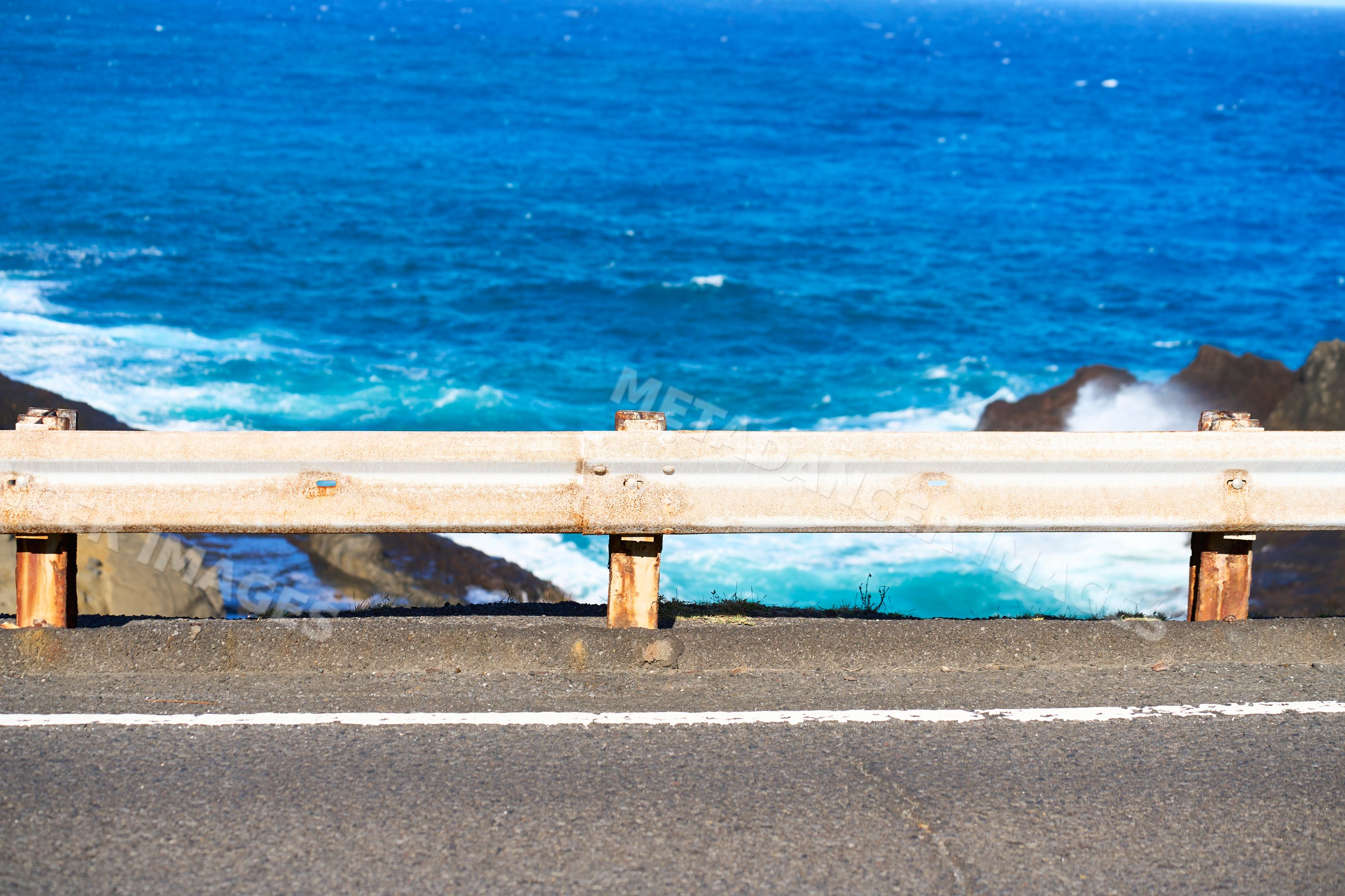 Coastal highway road with guardrail and ocean waves at shoreline
