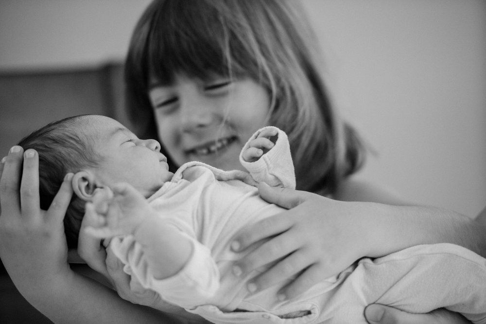 Newborn baby held by smiling young sibling indoors