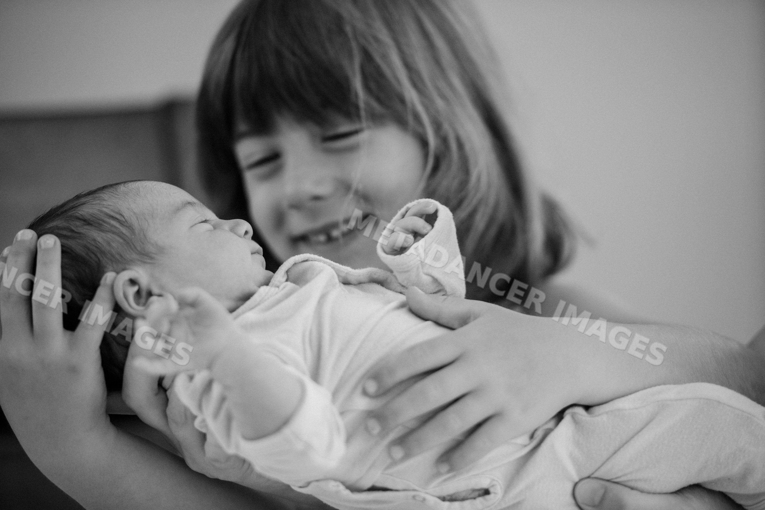 Newborn baby held by smiling young sibling indoors