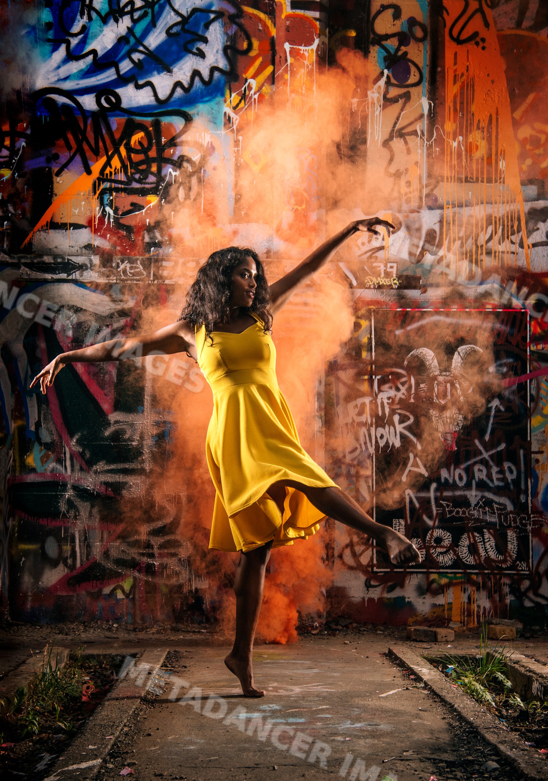 South Asian woman dancing with orange smoke in front of graffiti wall