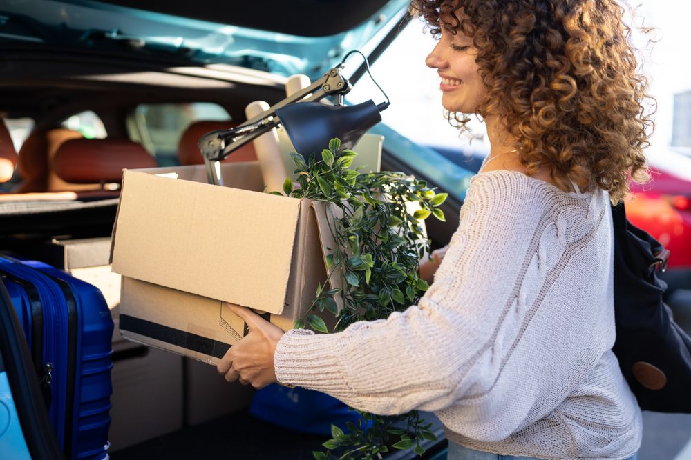 White woman loading box with plant and lamp into car trunk for moving