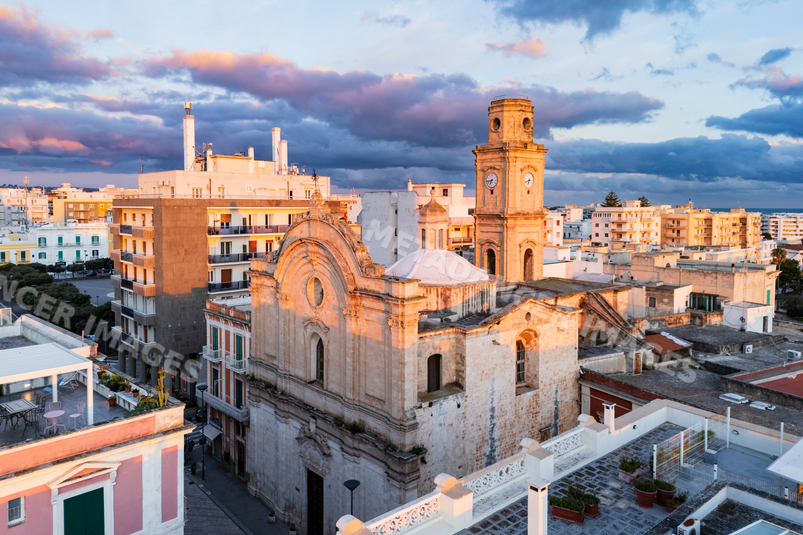 Church clock tower over rooftops at sunrise in monopoli, Italy