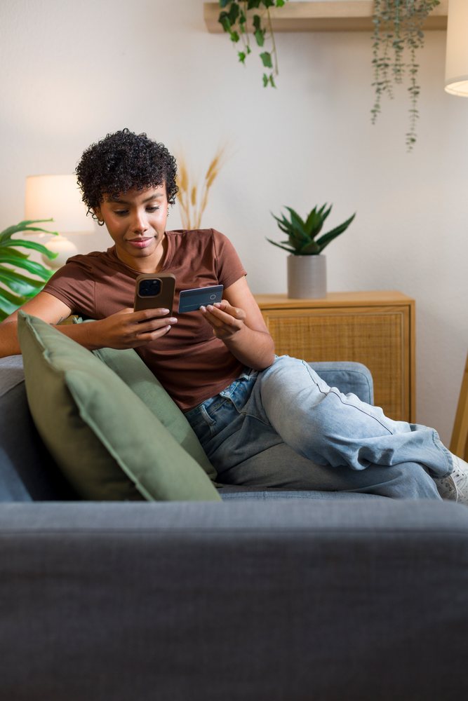 African American woman using mobile phone and credit card on couch