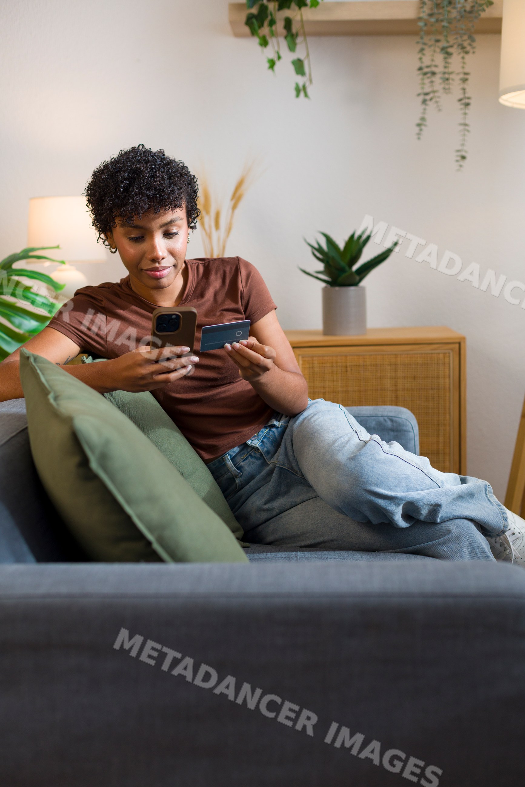 African American woman using mobile phone and credit card on couch