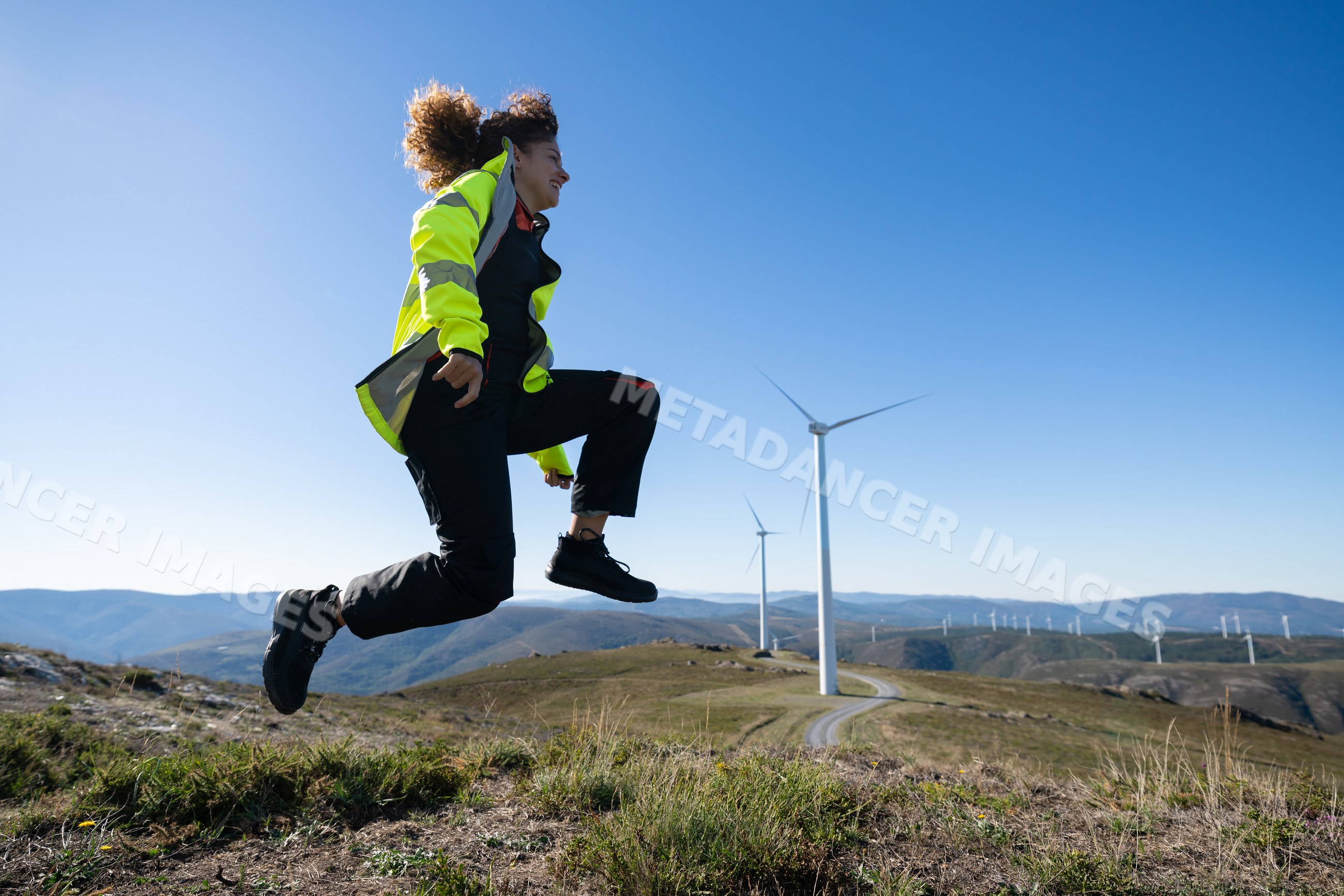 White woman jumping near wind turbines in Galicia mountains