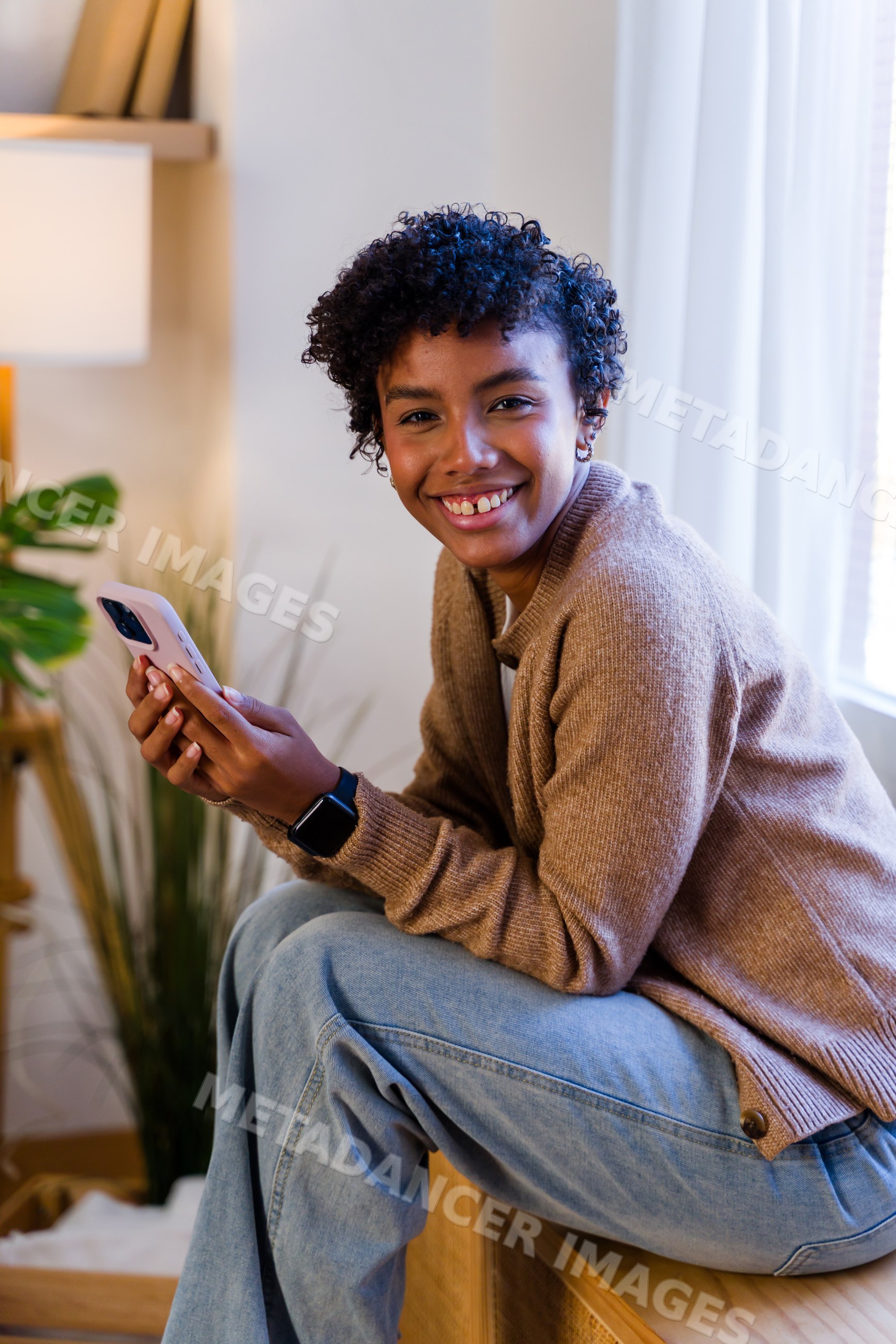 African American woman sitting indoors smiling and holding smartphone