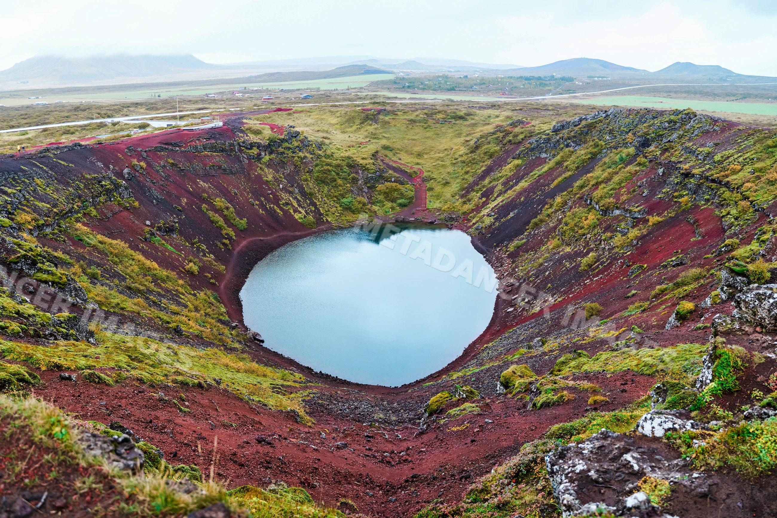 A scenic volcanic crater lake surrounded by red soil and green moss