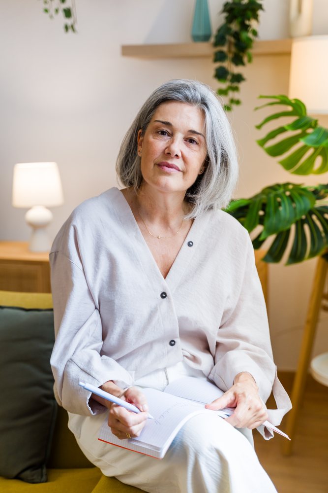 White woman sitting indoors writing in notebook in modern home