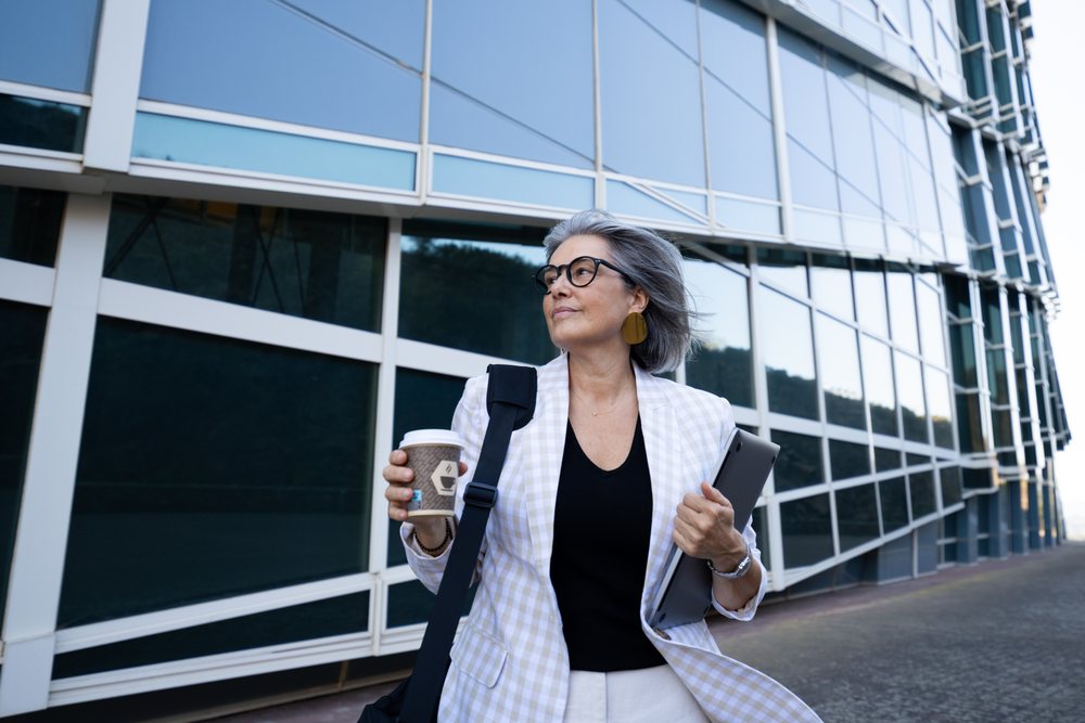 Businesswoman walking with coffee and tablet outside modern building