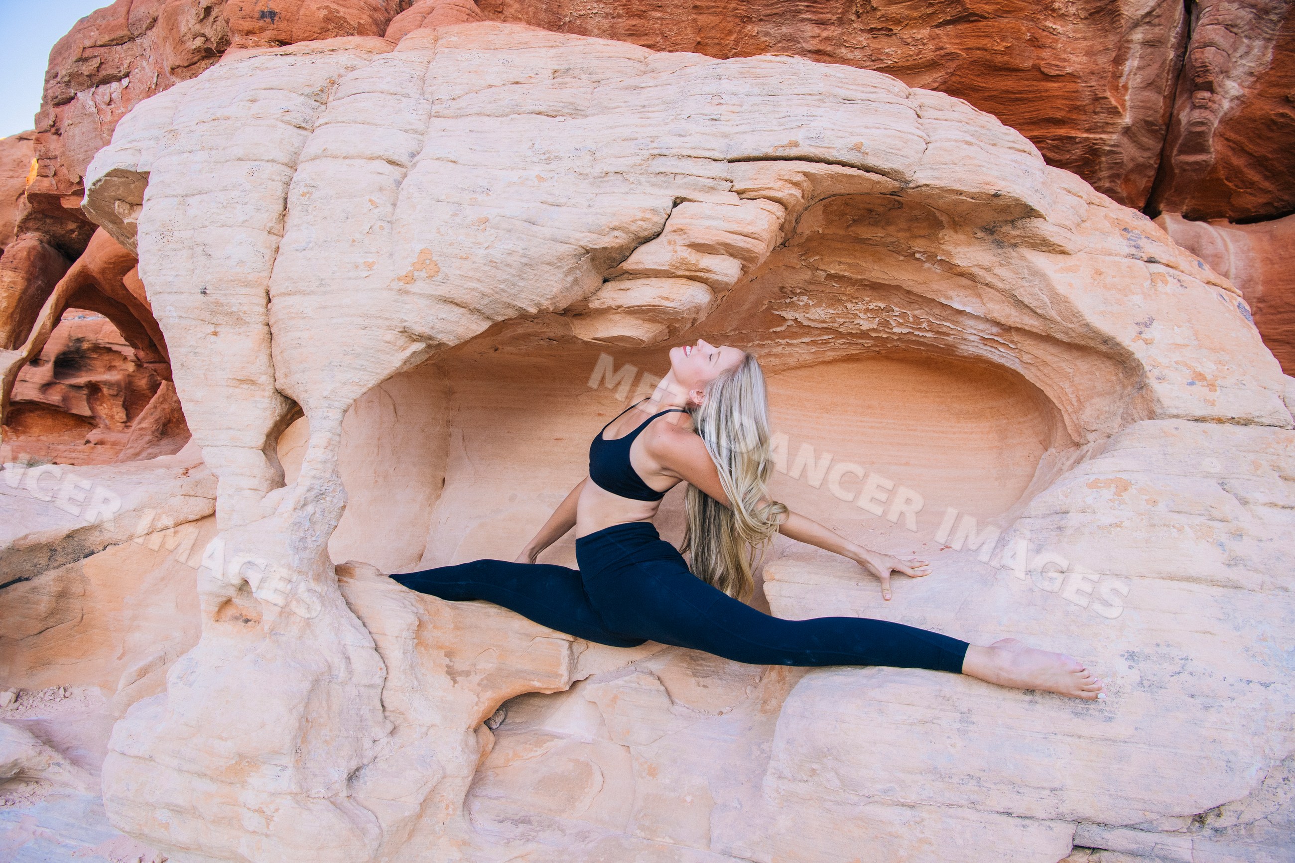White woman doing splits pose on rock formation outdoors