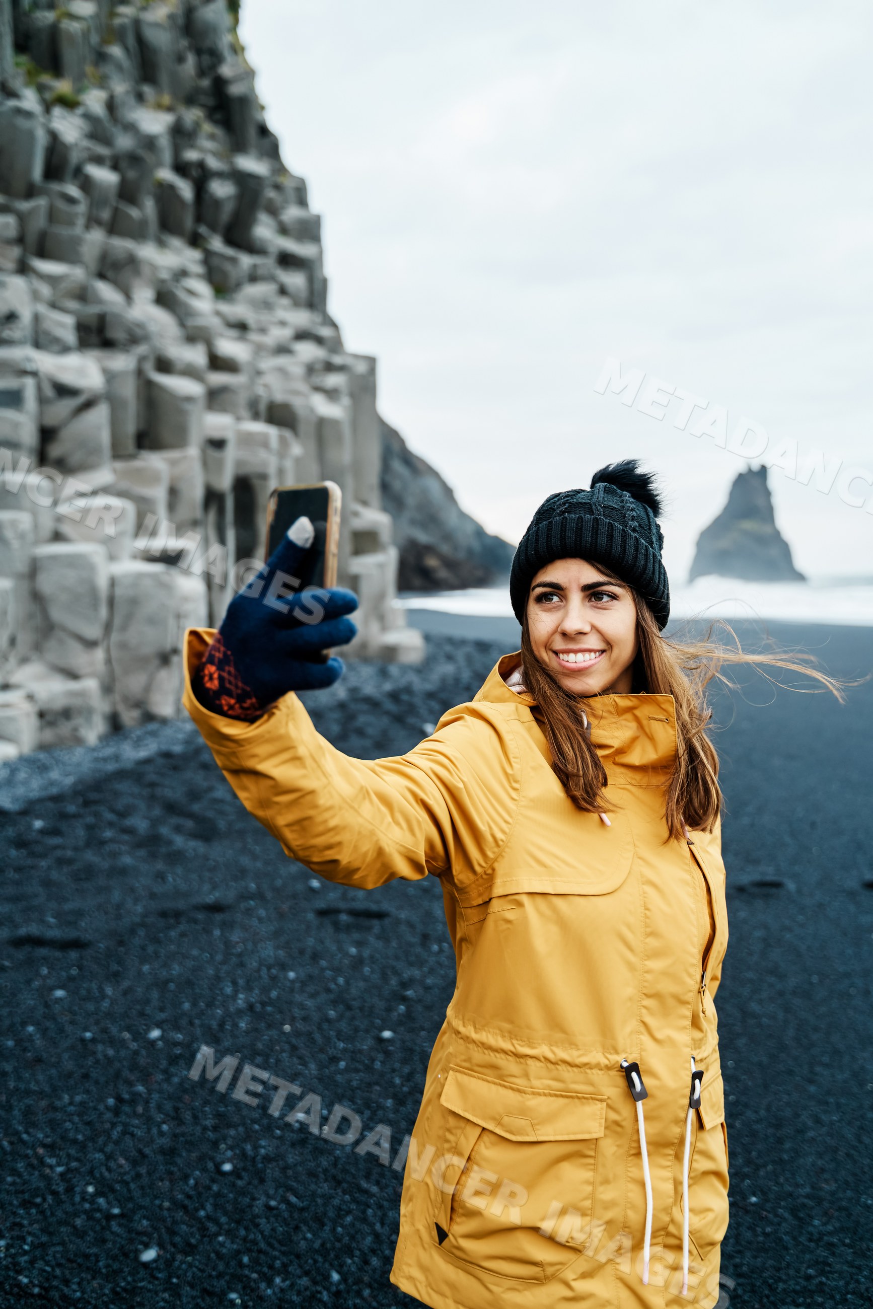 A white woman takes a selfie on a black sand beach in a beach