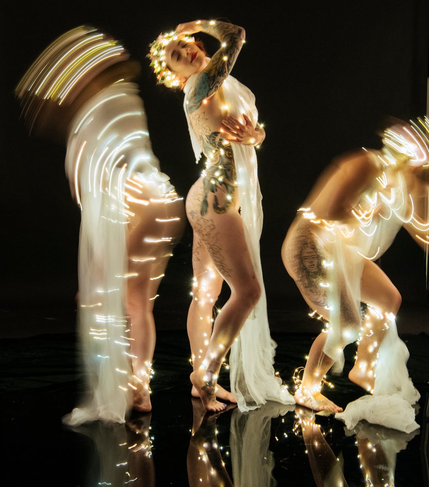 Three muses with tattoos posing artistically in fairy lights