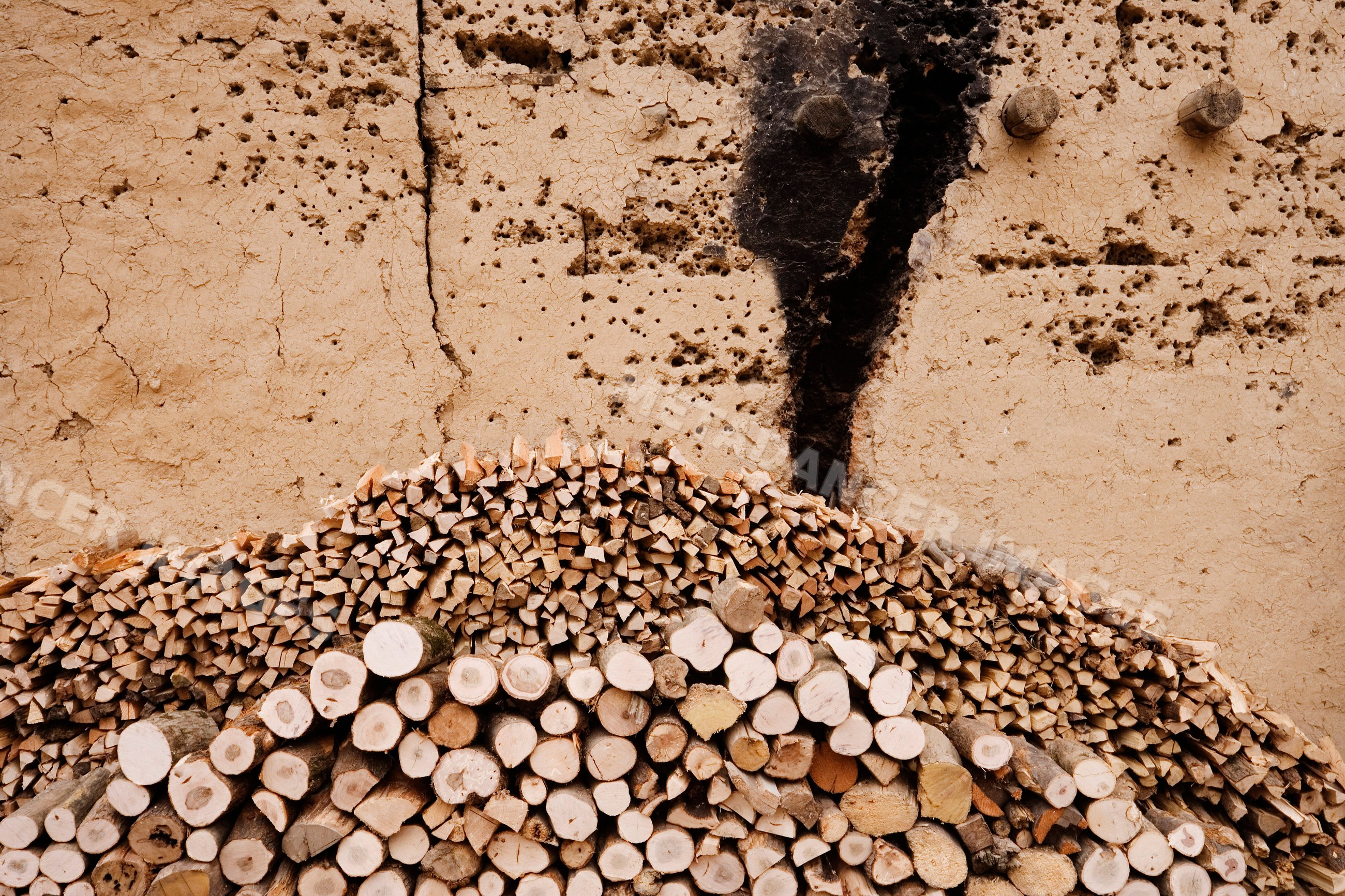 Stack of cut firewood arranged against cracked wall