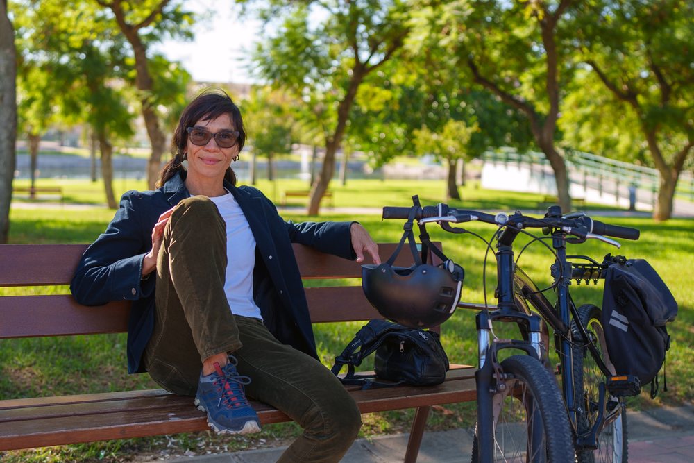Hispanic woman seated on bench with bicycle and helmet in Málaga park