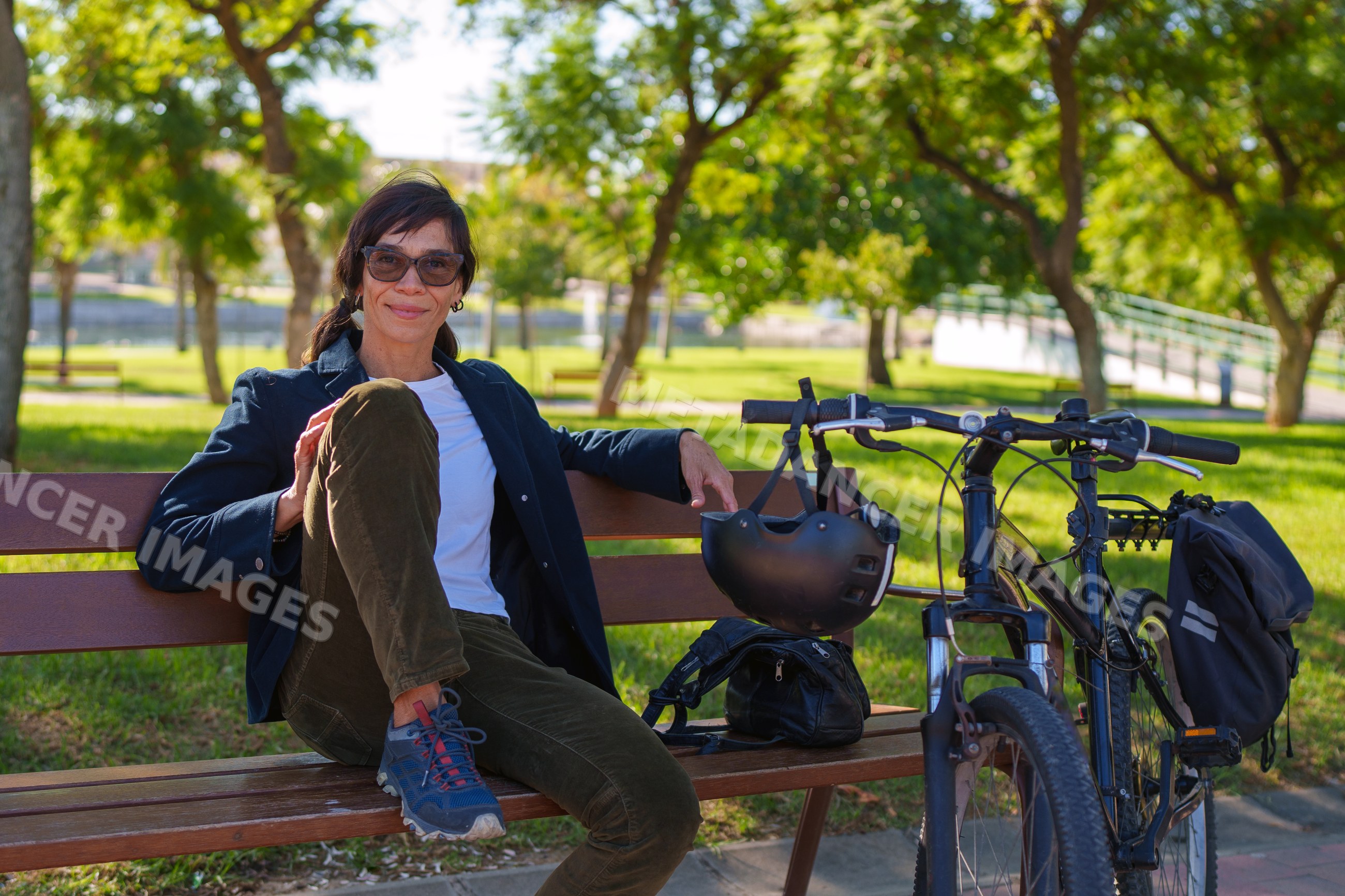 Hispanic woman seated on bench with bicycle and helmet in Málaga park