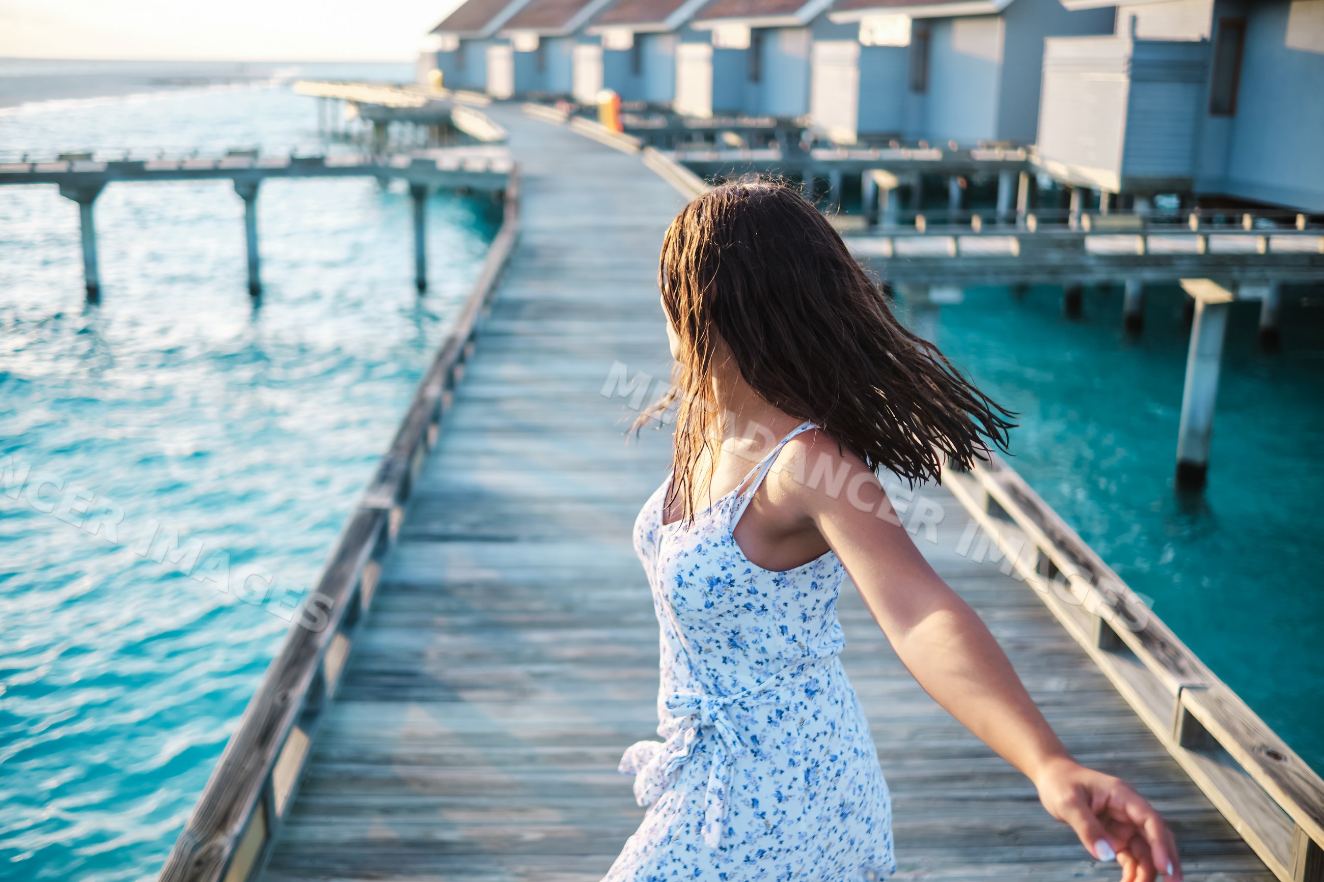 White Woman walking on a wooden pier by overwater bungalows