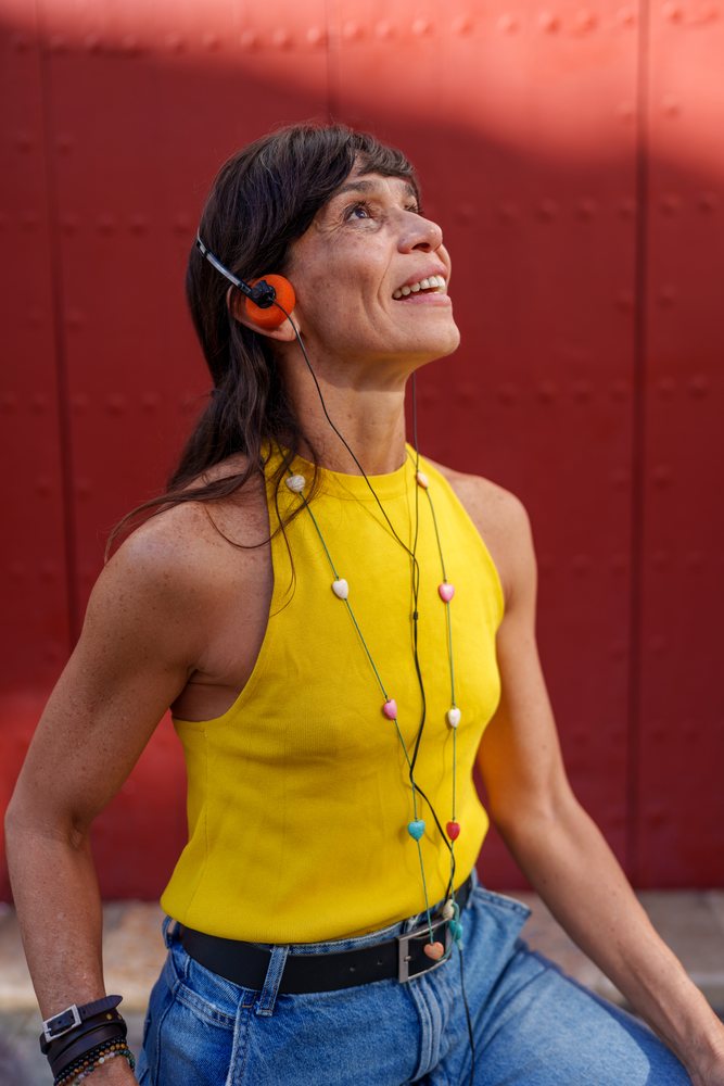 Hispanic woman listening to music with headphones against red metal
