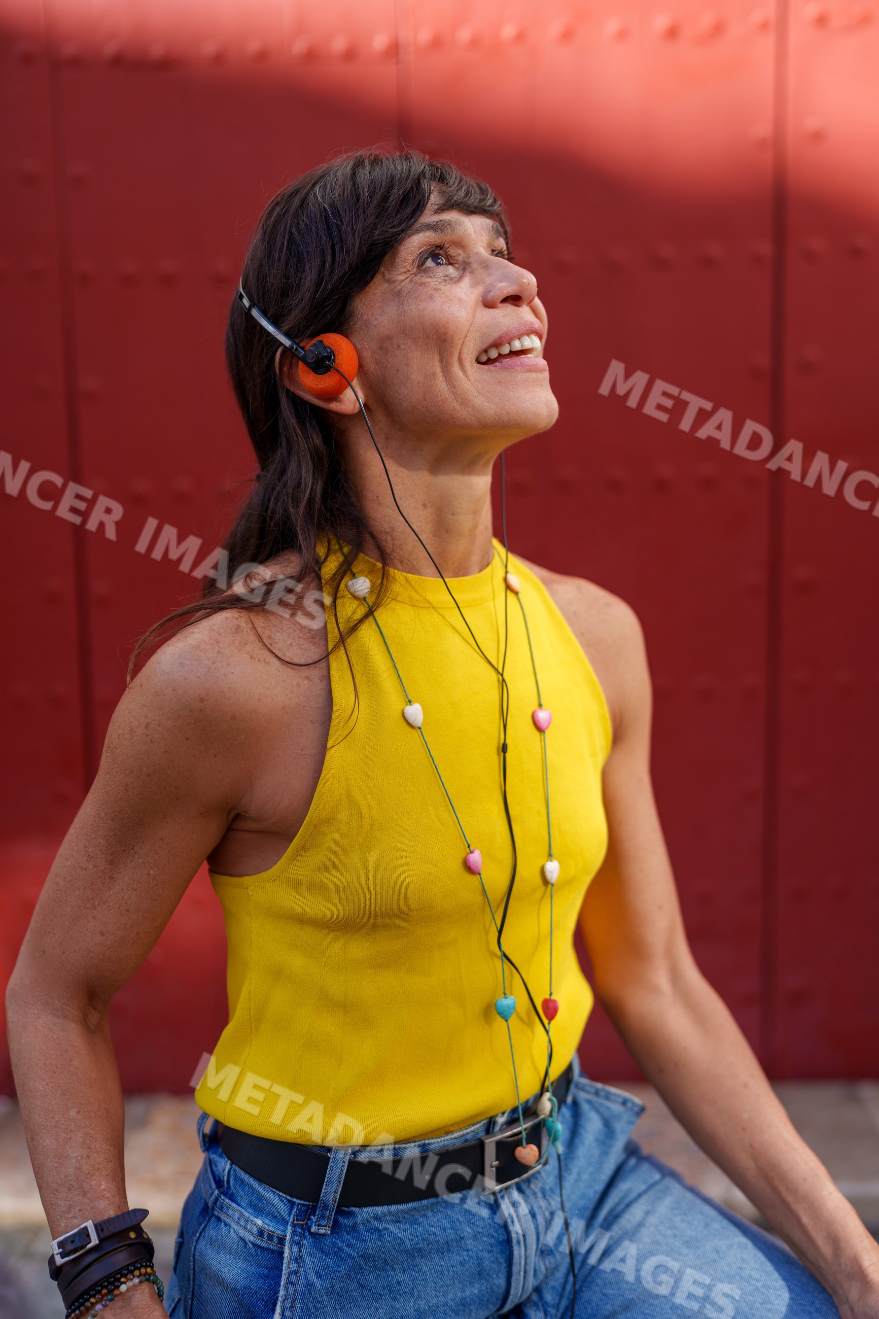 Hispanic woman listening to music with headphones against red metal