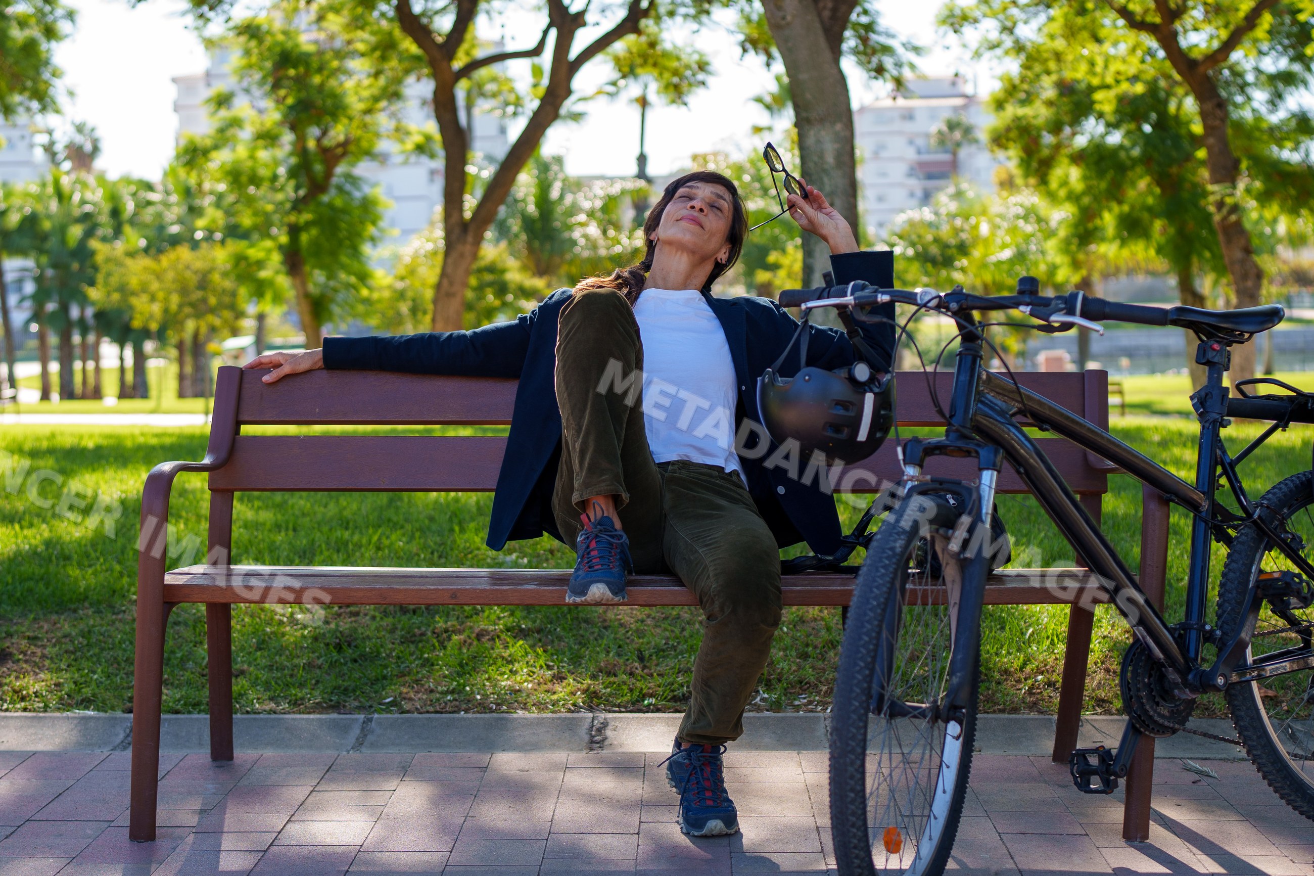 Hispanic woman resting on bench beside bicycle in Málaga park