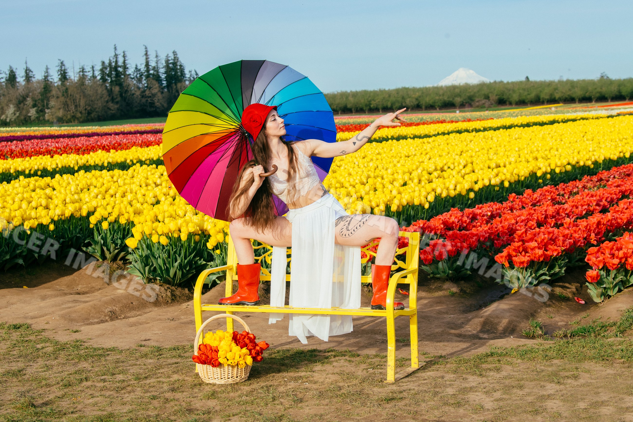 White woman with rainbow umbrella sitting on yellow bench