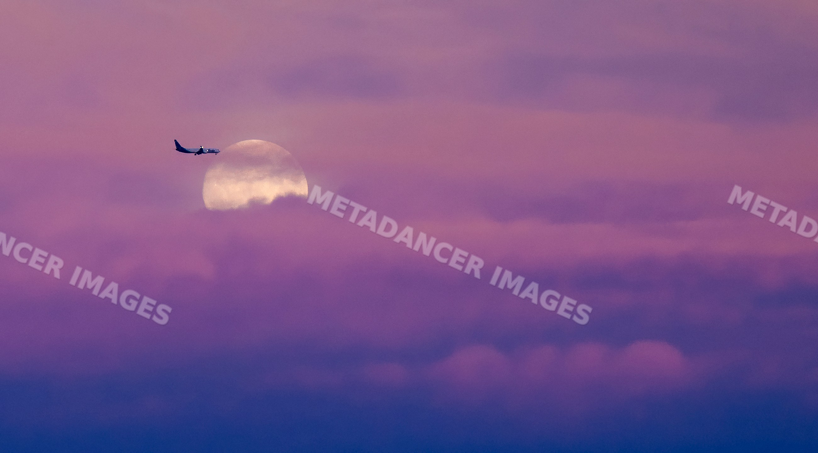 Aircraft flying past full moon in twilight sky with purple clouds