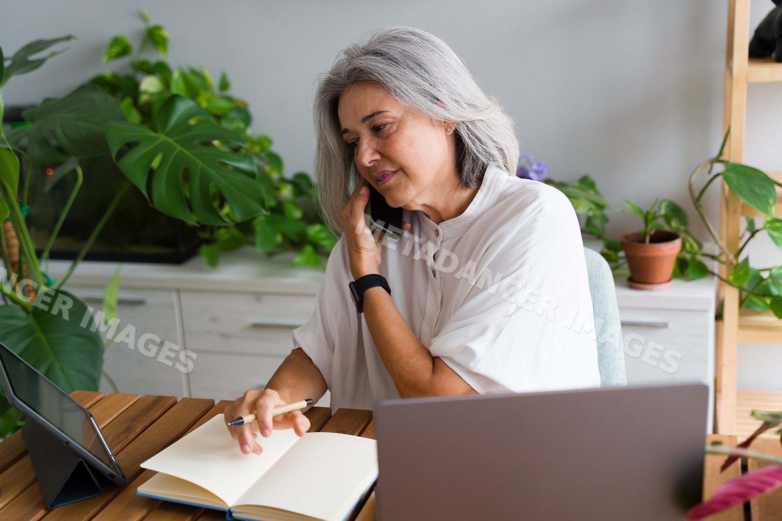 Mature white woman on phone working with notebook and laptop