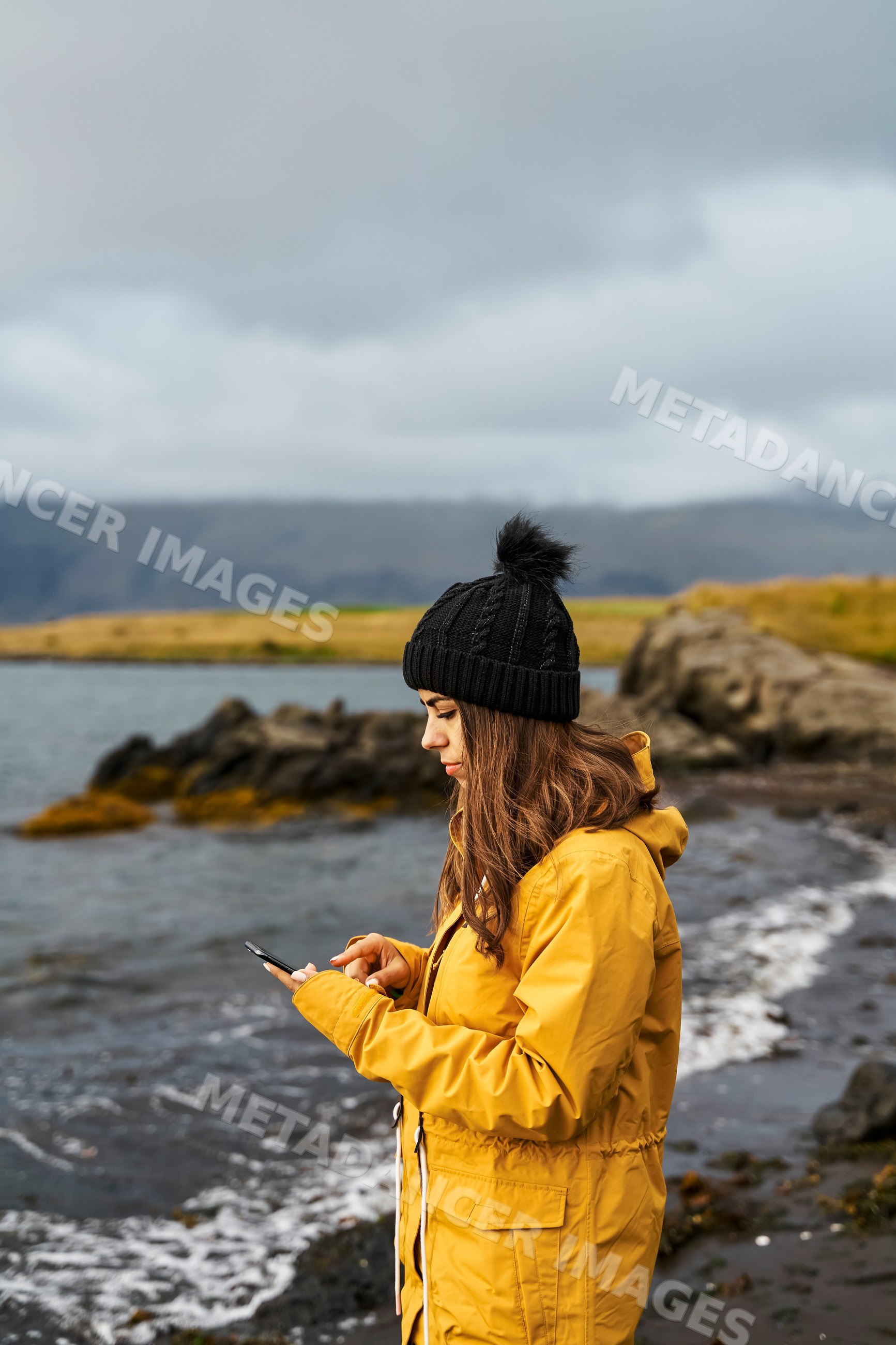 A white woman uses her smartphone by the rocky shoreline