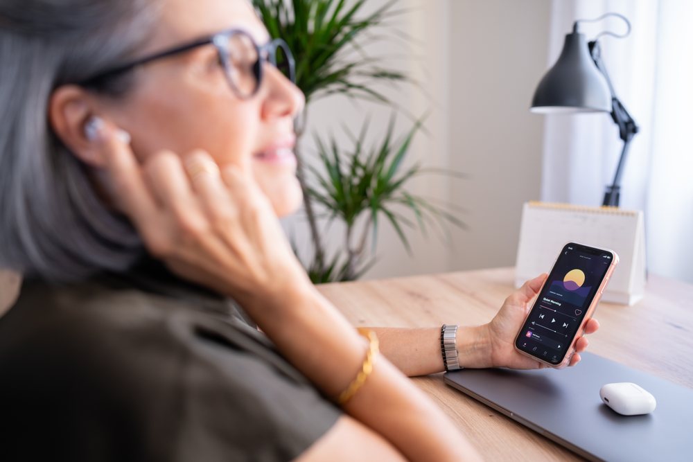 White woman listening to music on wireless earbuds holding smartphone