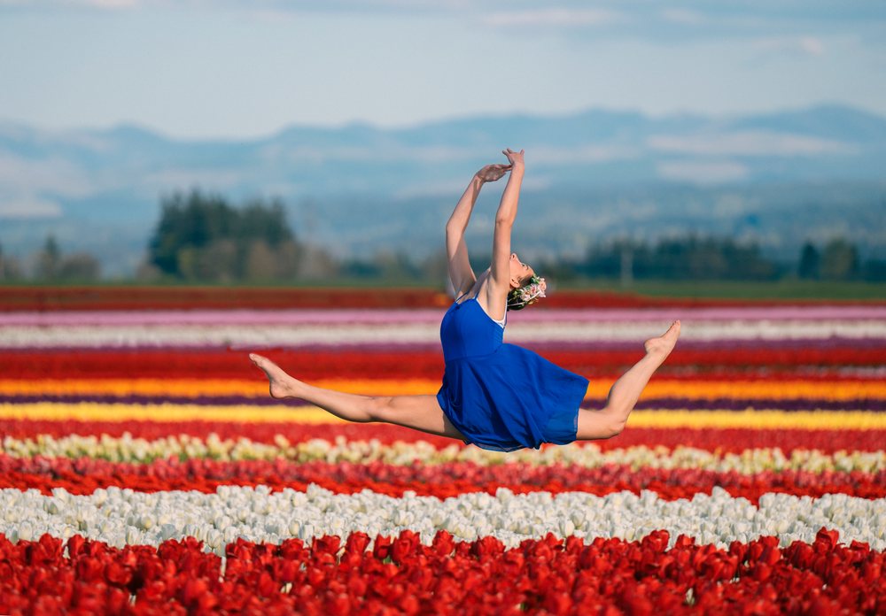 Ballet white dancer leaping over colorful tulip field outdoors
