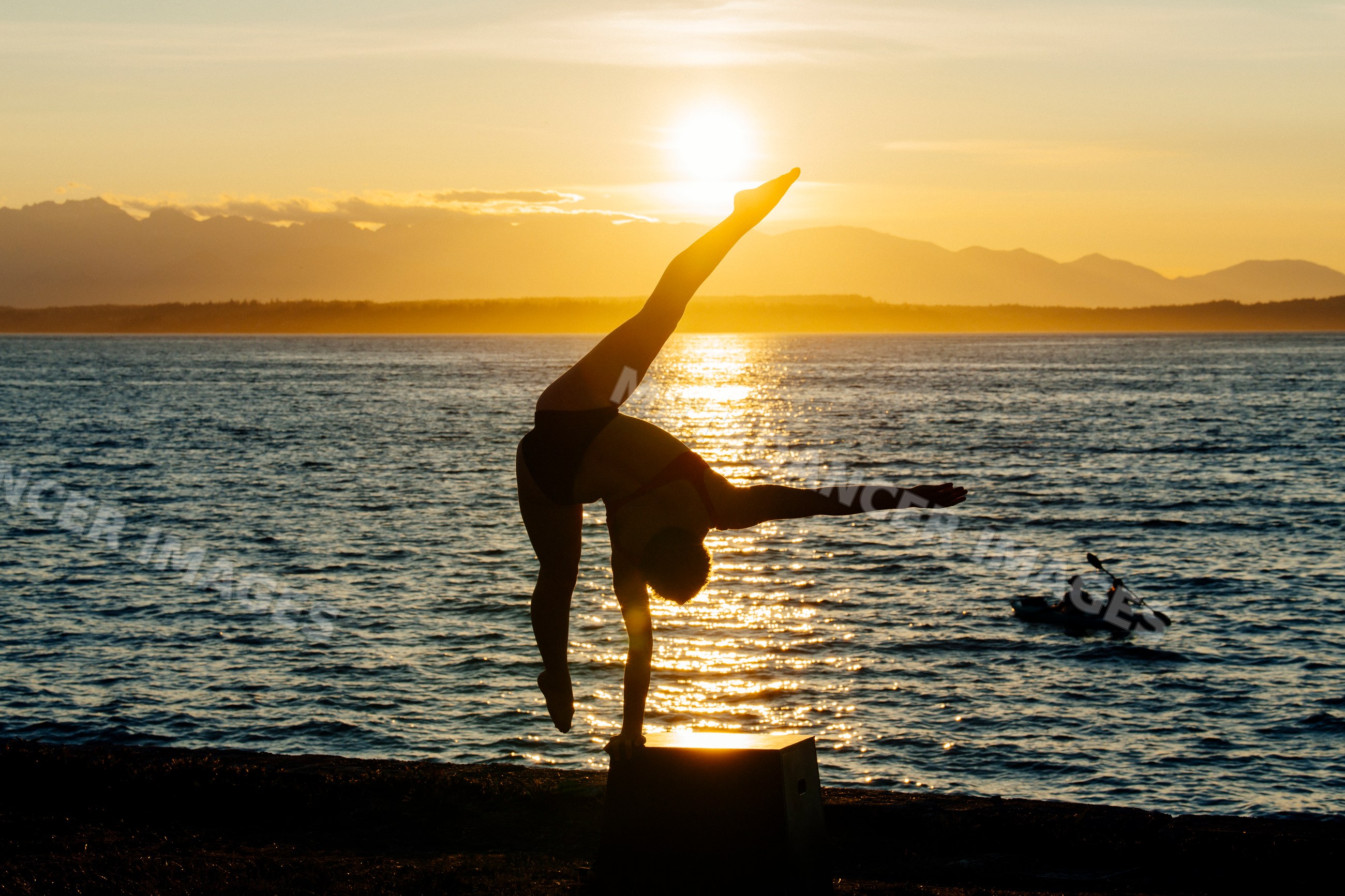 White person doing handstand near ocean at sunset with kayak, USA