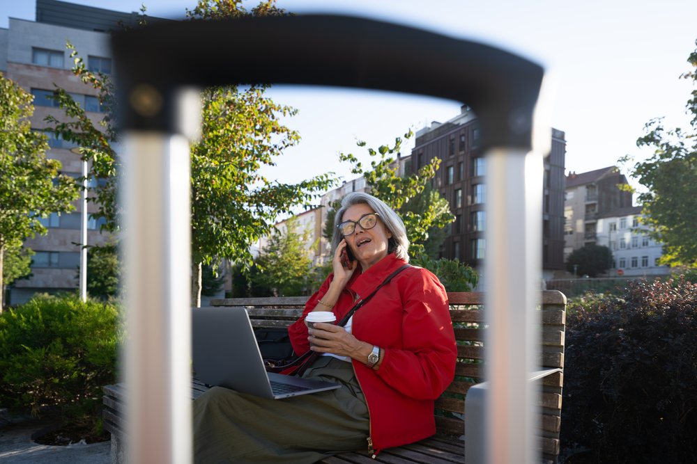 White woman talking on phone with laptop and coffee in urban park