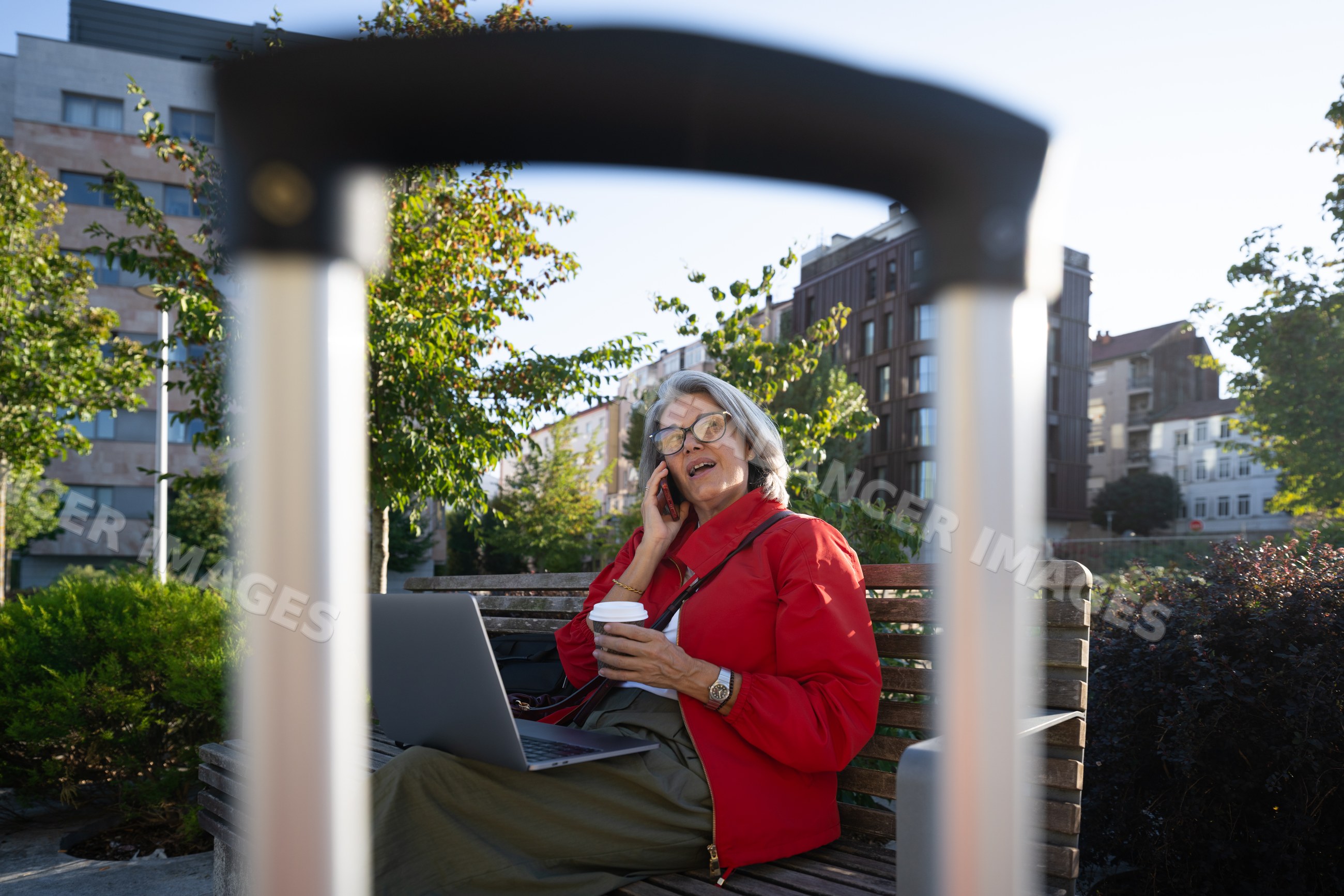 White woman talking on phone with laptop and coffee in urban park