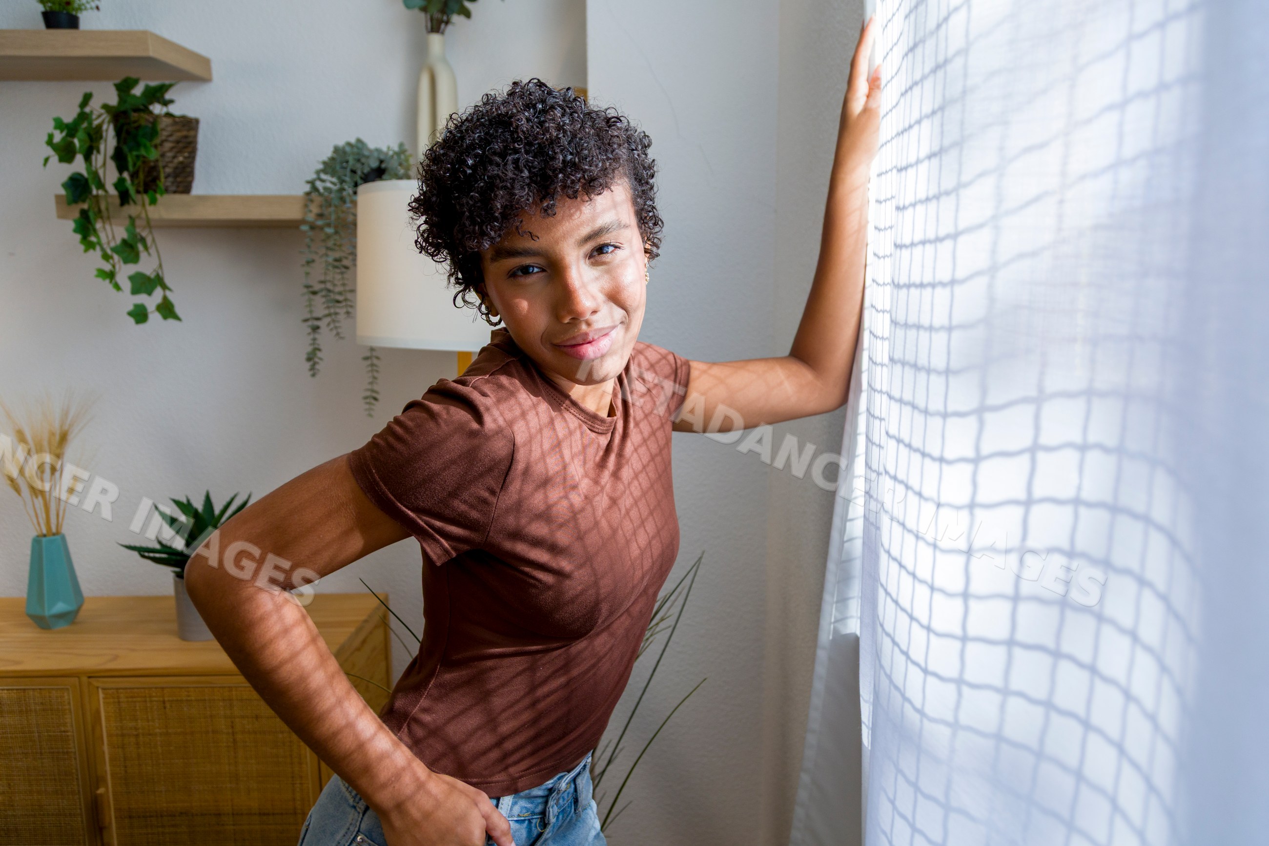 Young African American woman standing by window with white curtains