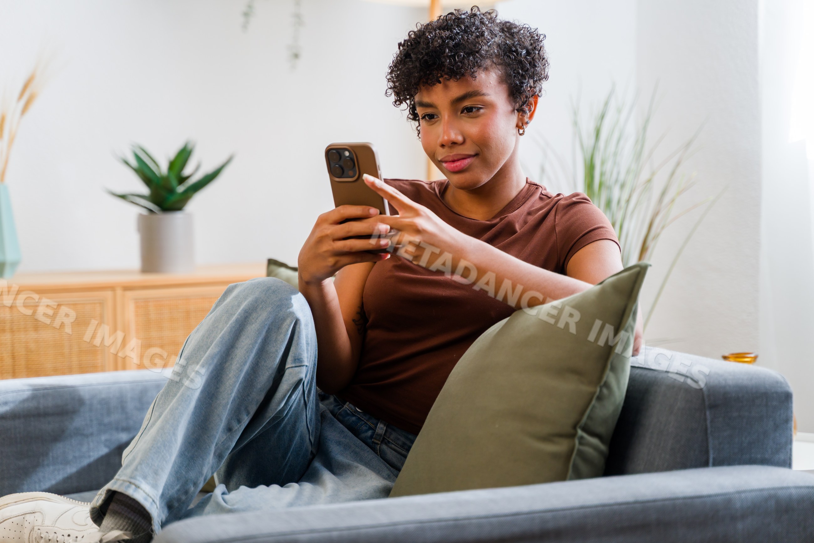 African American woman sitting on sofa using smartphone in living room