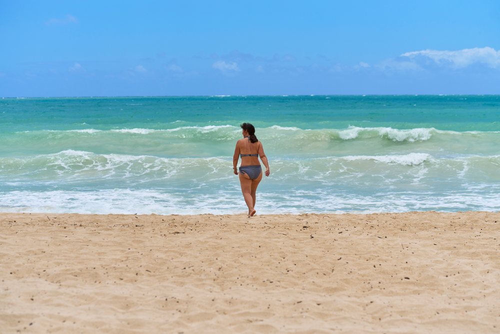 White woman walking on beach with ocean waves in a beach