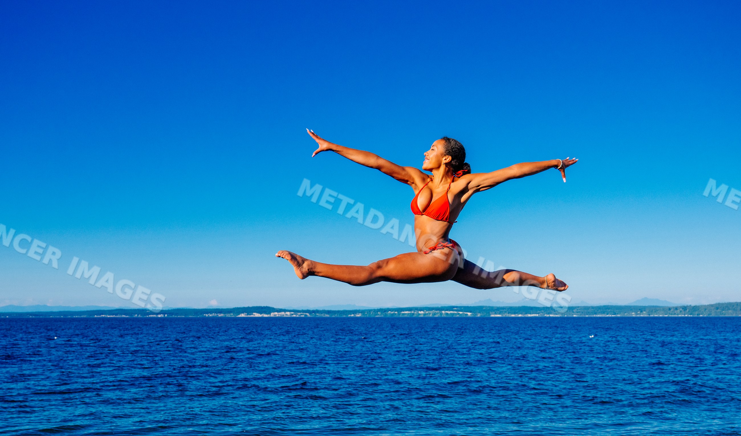 Woman in red swimwear jumping over ocean water on a clear day