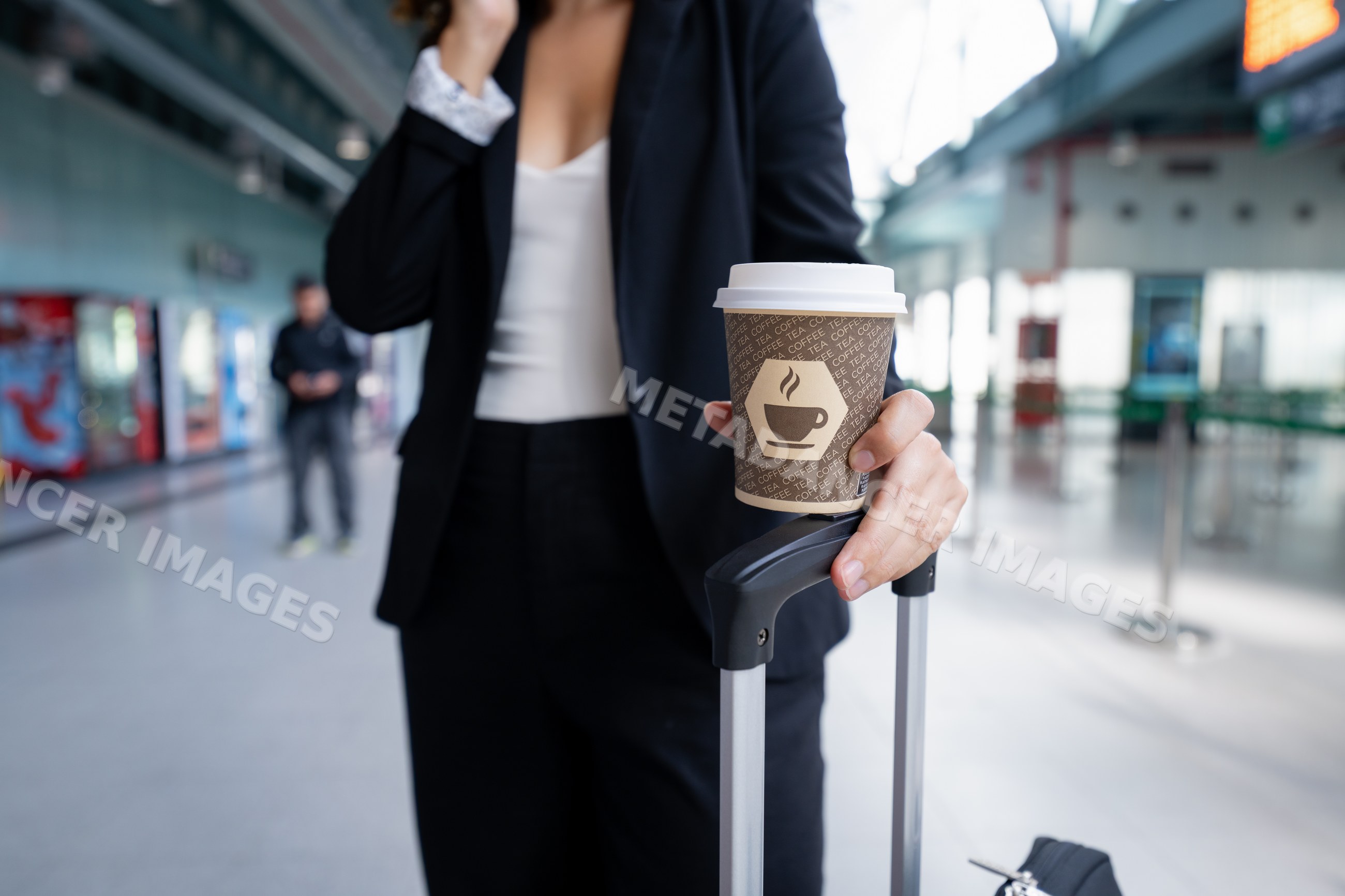 White woman holding coffee cup and luggage handle in airport terminal