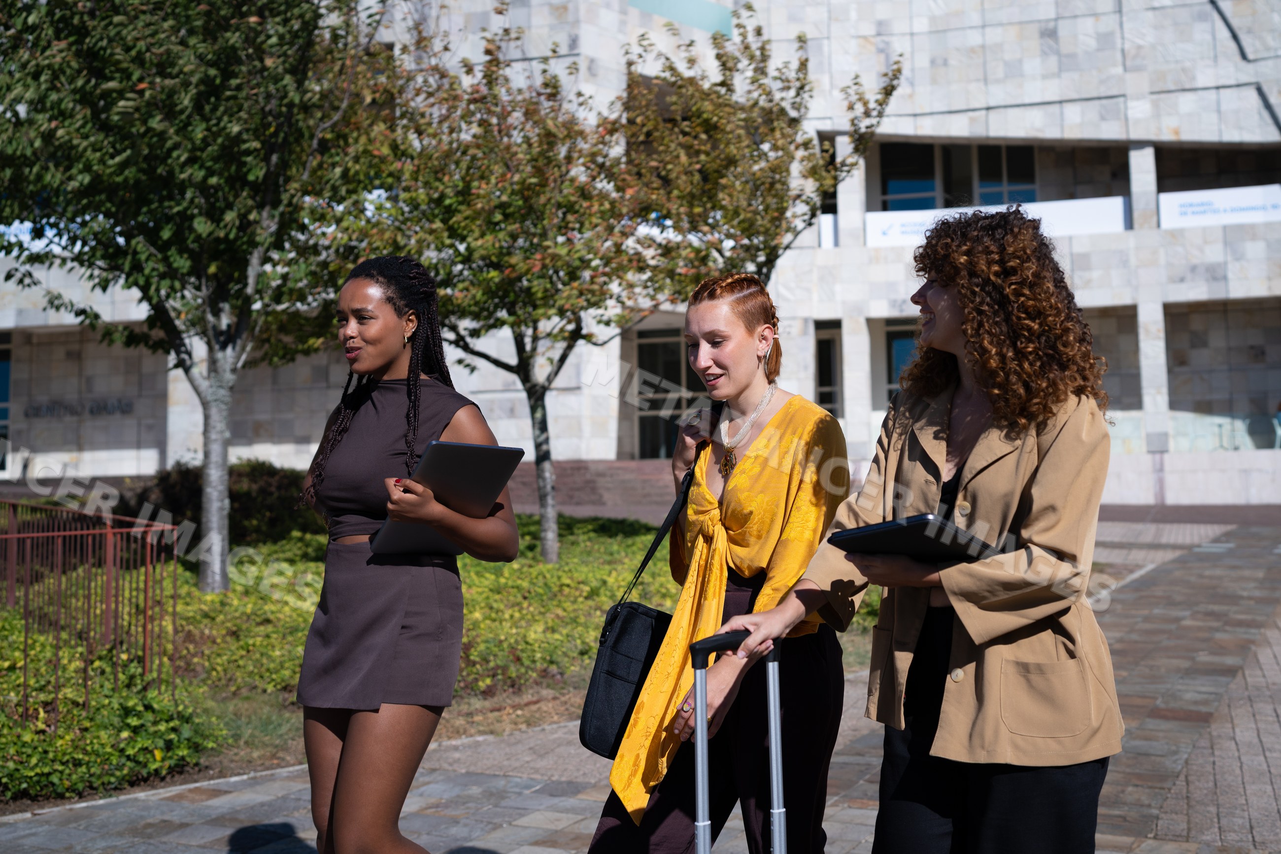 Three African American and white women walking outdoors with tablets