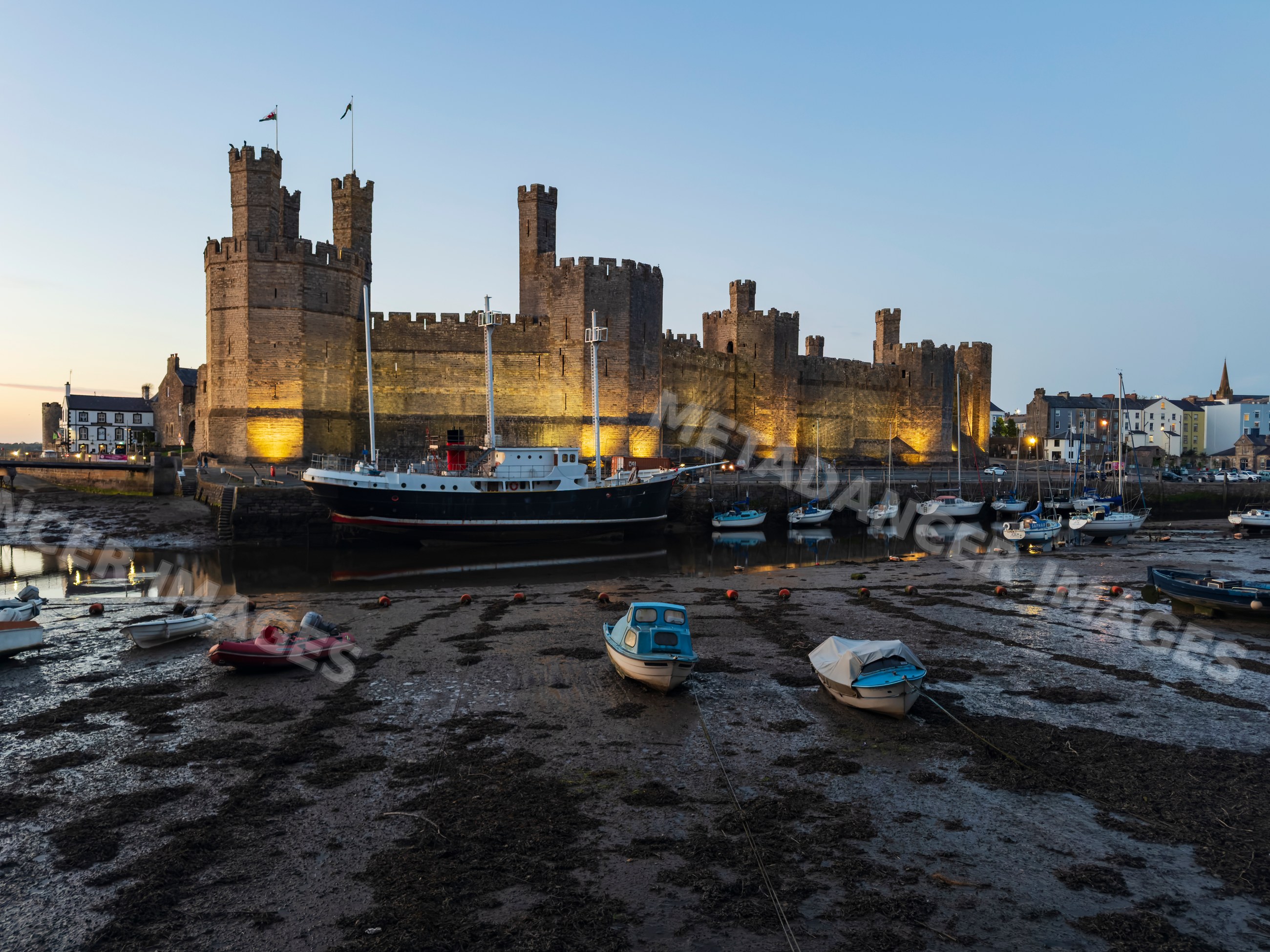 Caernarfon castle at evening with boats moored in welsh harbor