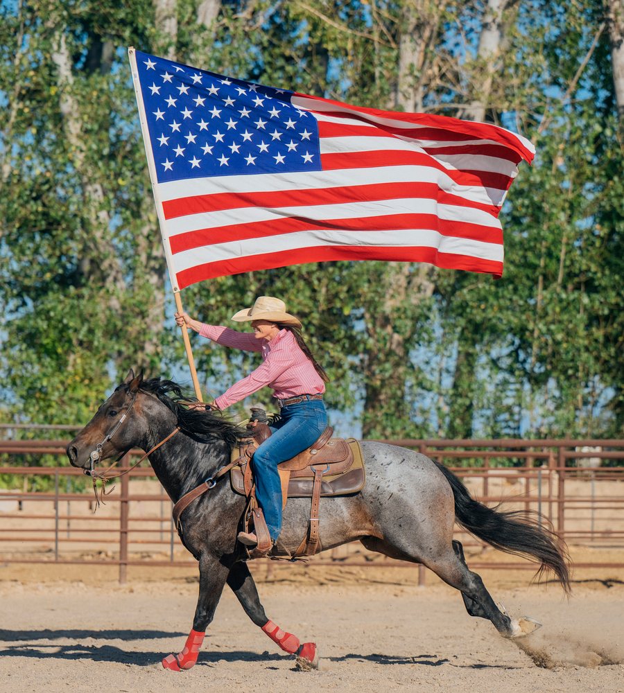 White woman horseback riding with american flag in outdoor arena