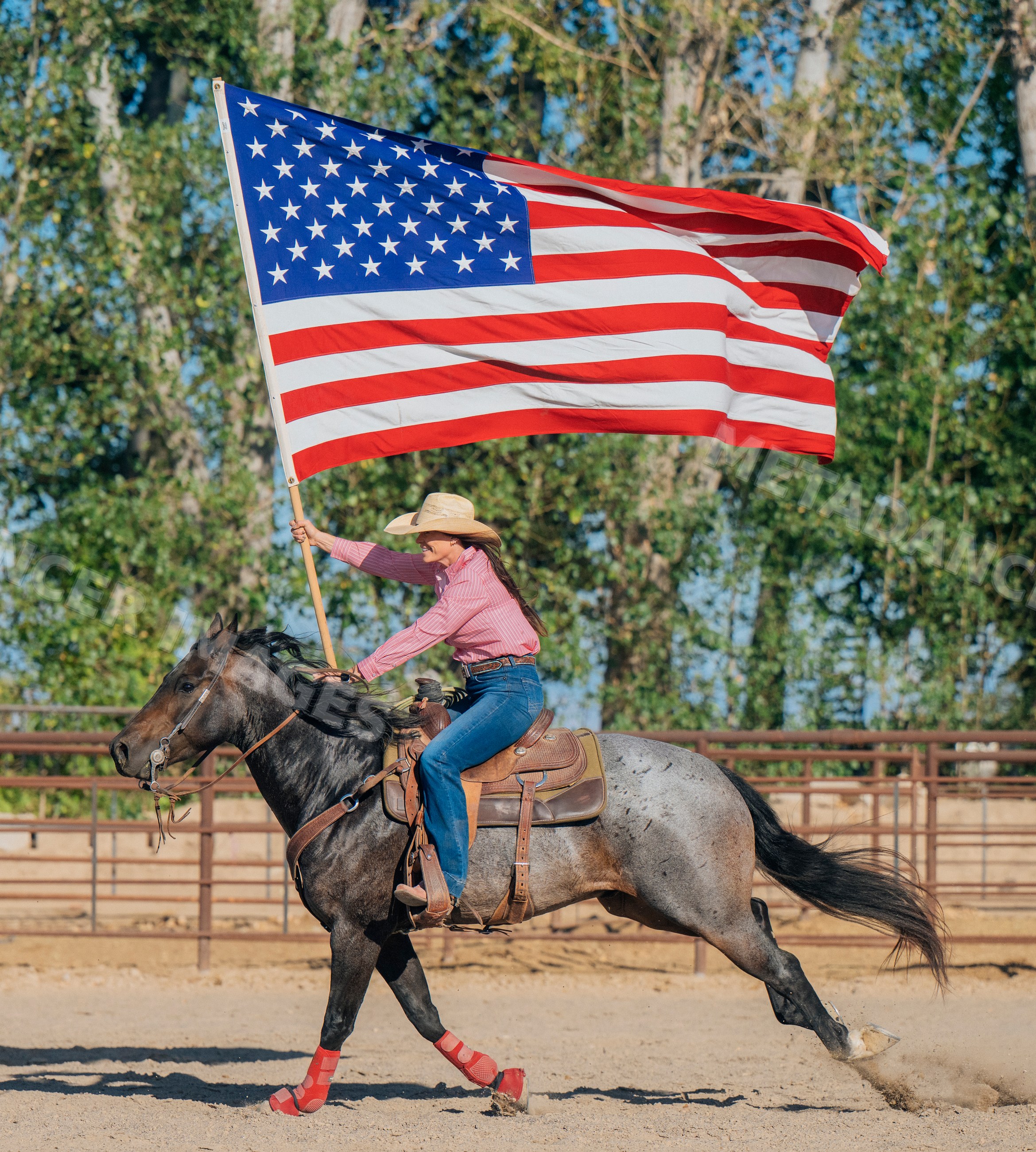 White woman horseback riding with american flag in outdoor arena