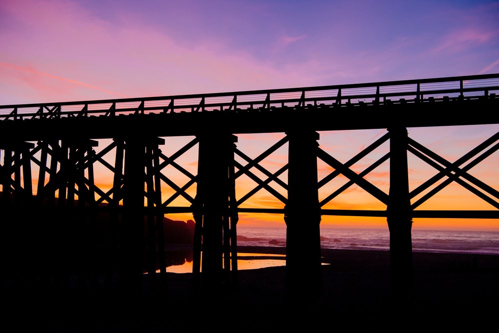 Wooden bridge silhouette at sunset over ocean beach