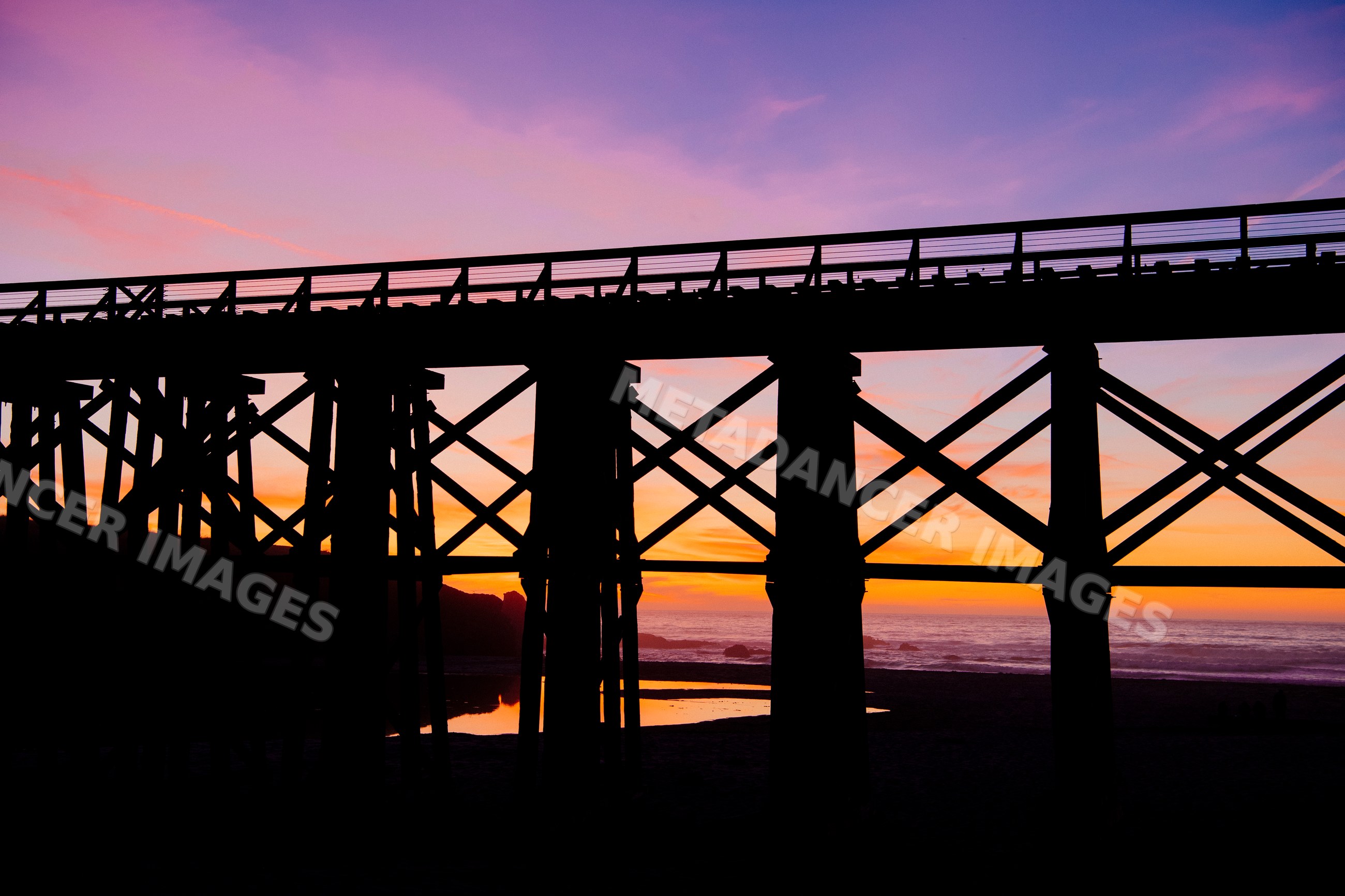 Wooden bridge silhouette at sunset over ocean beach